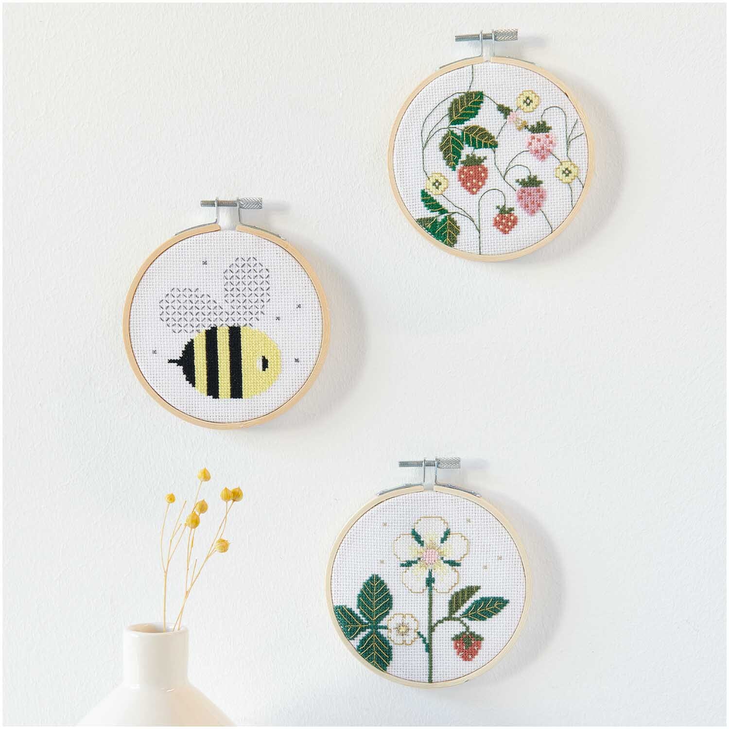 Stickpackung Bild Biene Ø10cm: Drei Stickrahmen mit Bienen- und Blumenmotiven von Rico Design an einer weißen Wand.