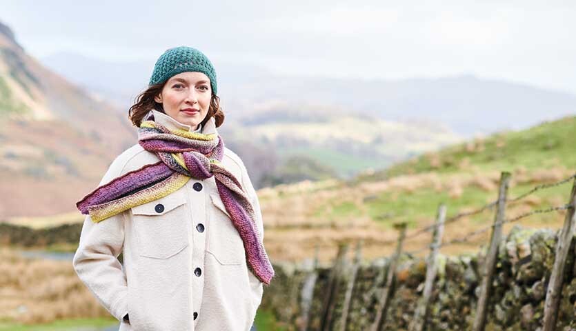 Strickanleitung Schal aus Creative Alpaca Dégradé Lucky 8: Frau mit buntem Schal in ländlicher Landschaft.