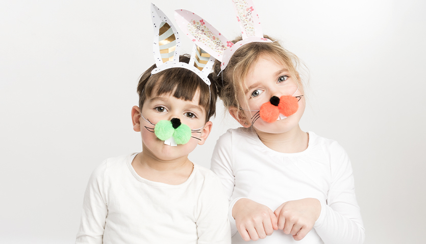 Bastelanleitung Hasenohren aus Papier: Zwei Kinder tragen weiße Hasenohren und bunte Nasen.