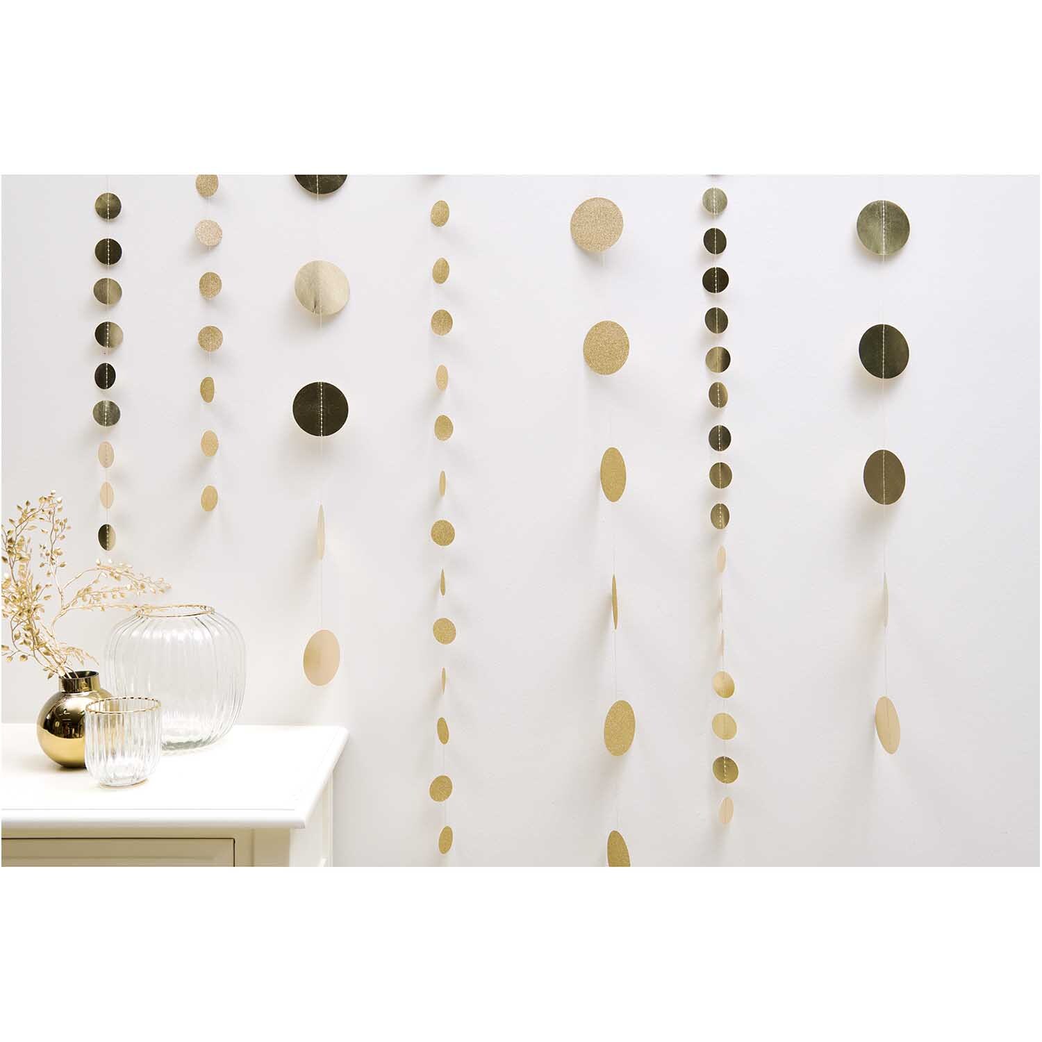 Genähte Girlande Kreise 8cm Glitter-gold 1,7m von Rico Design, dekorativ an einer weißen Wand hängend. Ideal für festliche Anlässe.