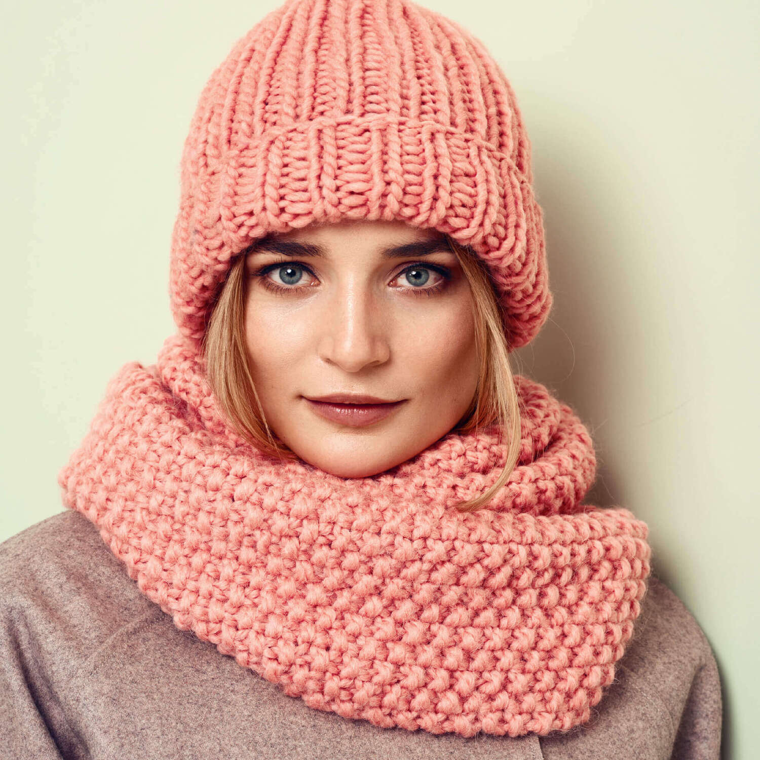 Strickanleitung Perlmuster Loop und Rippenmuster Mütze: Frau trägt rosa gestrickte Mütze und passenden Loop-Schal, stilvoll und warm.