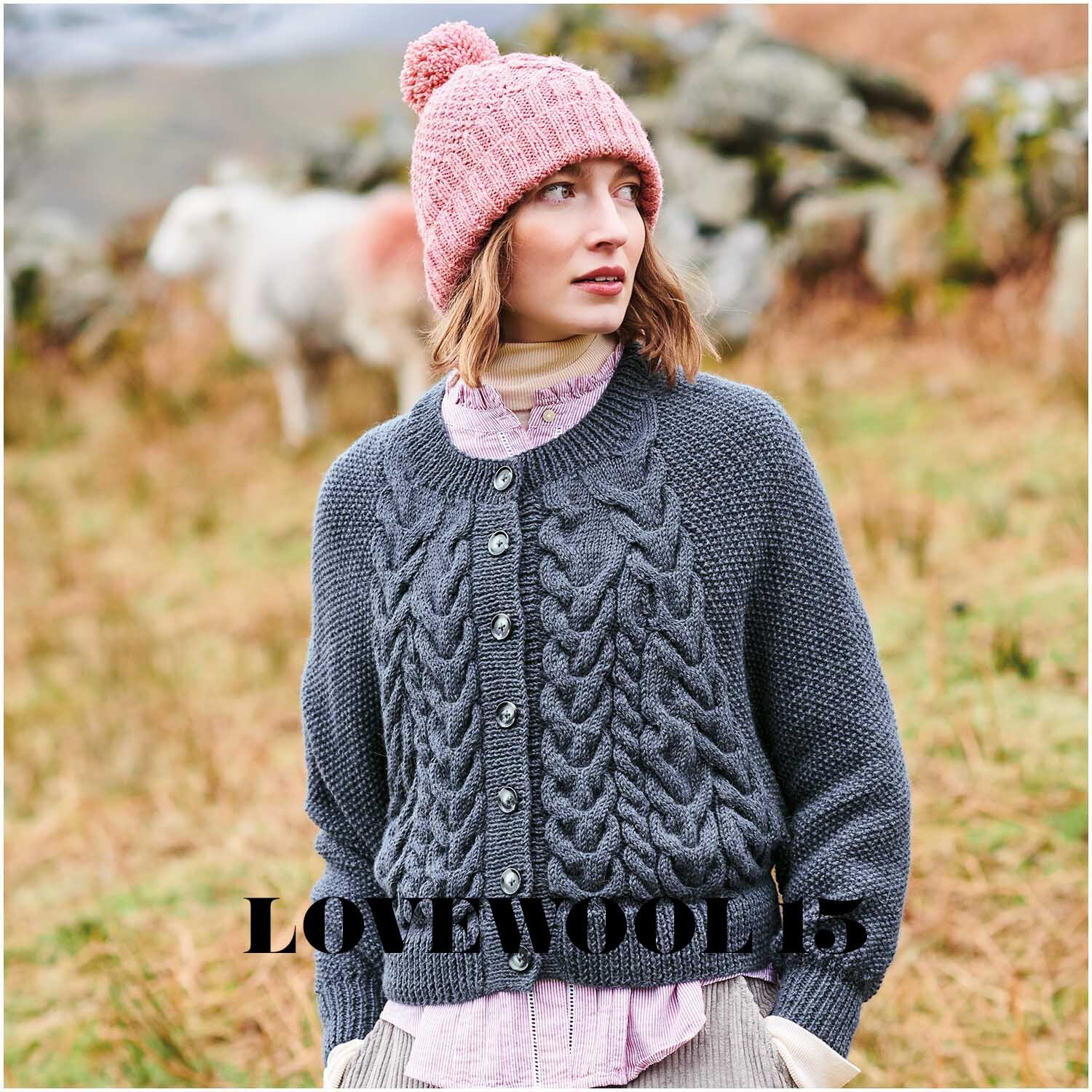 Essentials Baby Alpaca & Merino aran: Frau in marineblauer Strickjacke und rosa Mütze in ländlicher Umgebung.