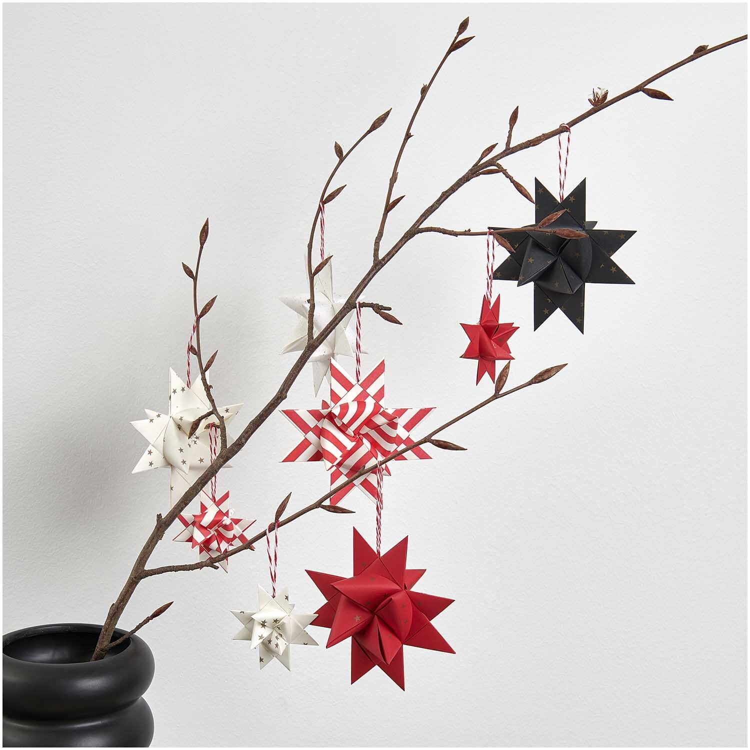 Paper Poetry Fröbelstreifen: Origami-Sterne in Schwarz, Rot und Weiß an einem Ast hängend.