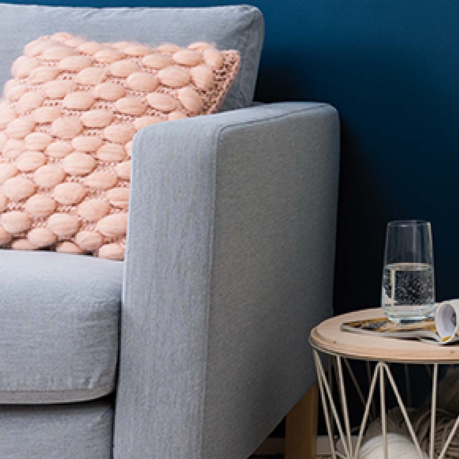 Anleitung Wellen-Webkissen auf einem grauen Sofa vor einer blauen Wand, daneben ein Tisch mit Glas.