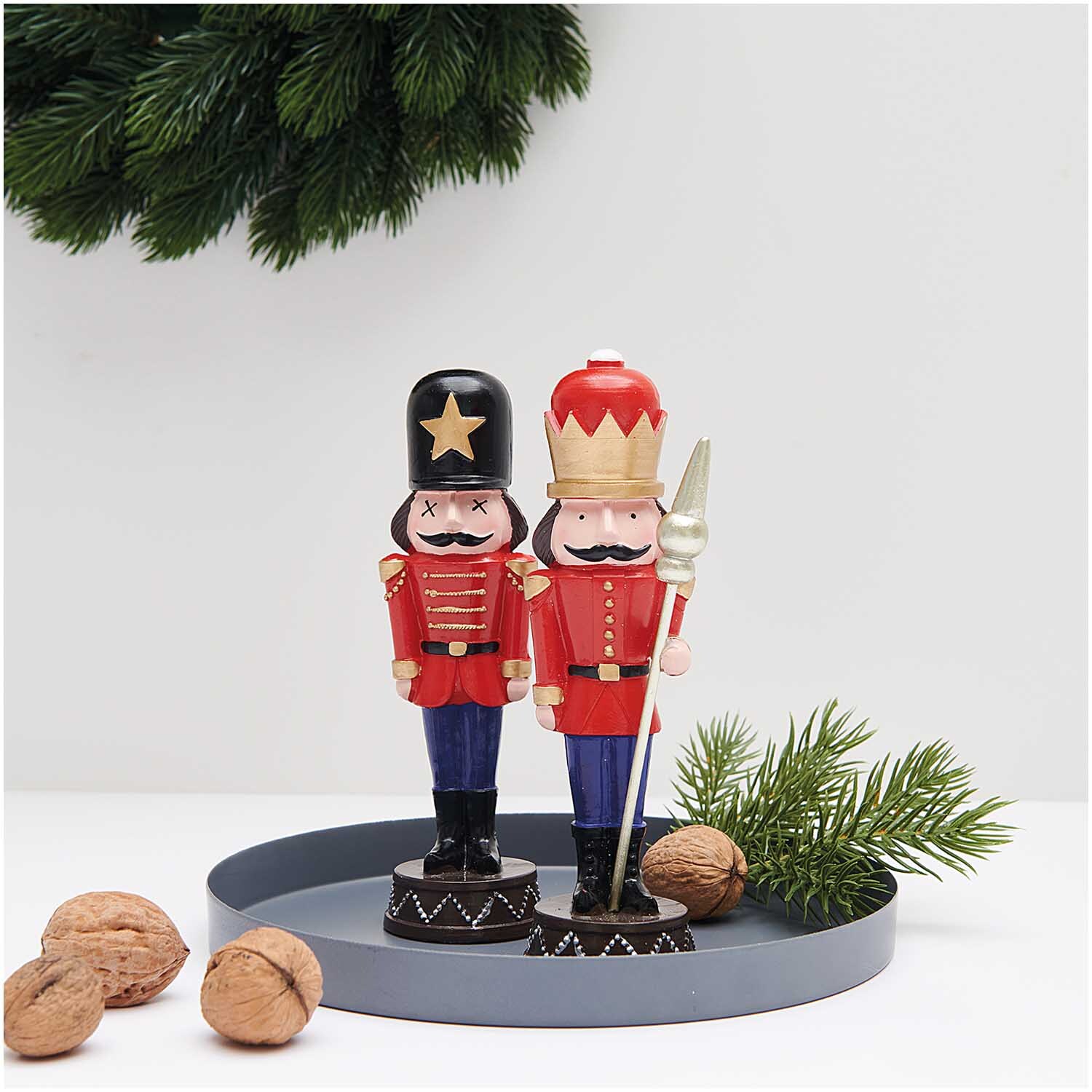 Polyresin Figur Nussknacker mit Stab 17cm: Zwei rote Nussknacker auf Tablett, umgeben von Tannenzweigen und Nüssen.