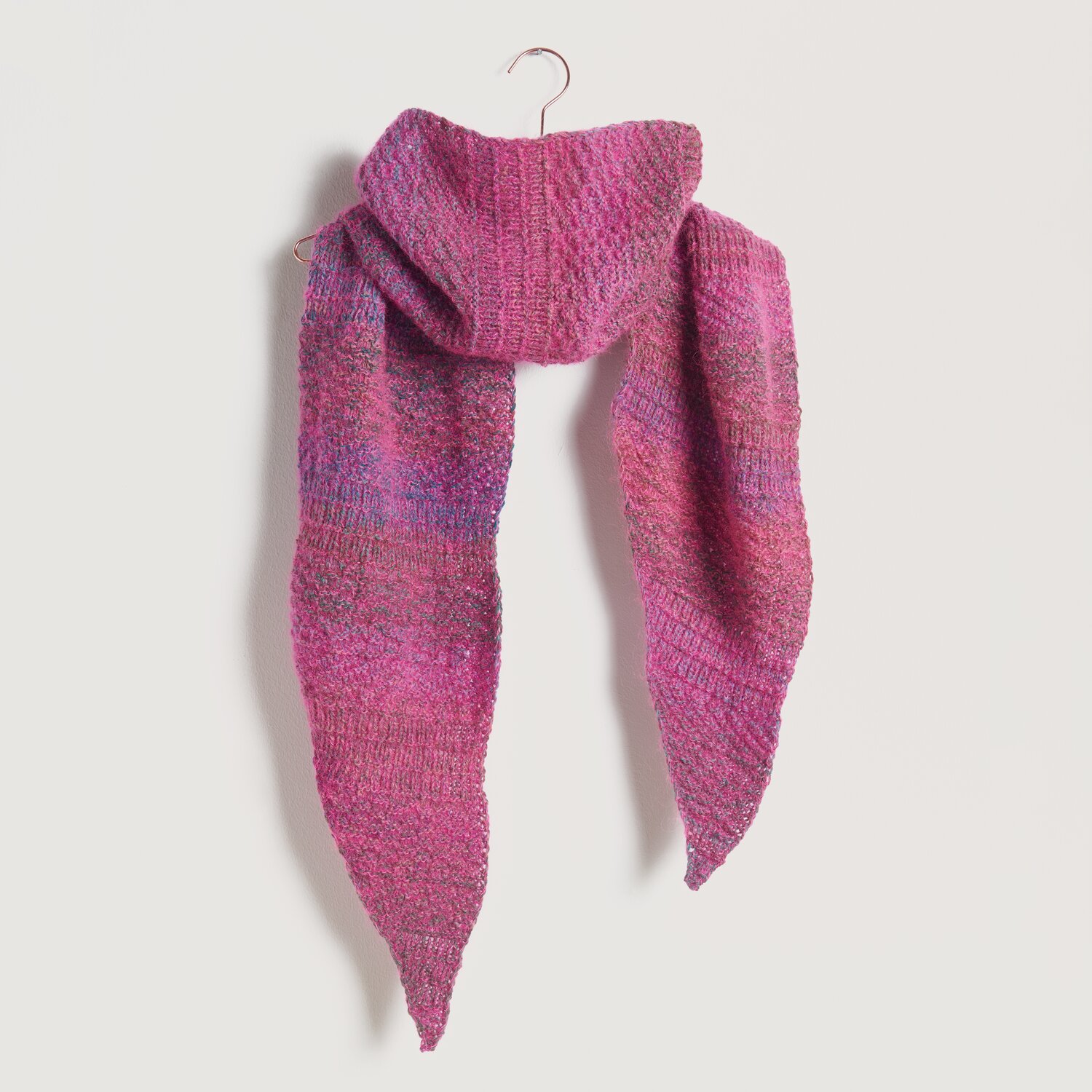 Strickset Tuch Modell 20a: Ein handgestricktes, mehrfarbiges Tuch in Rosa- und Lilatönen, elegant drapiert an einem Haken.
