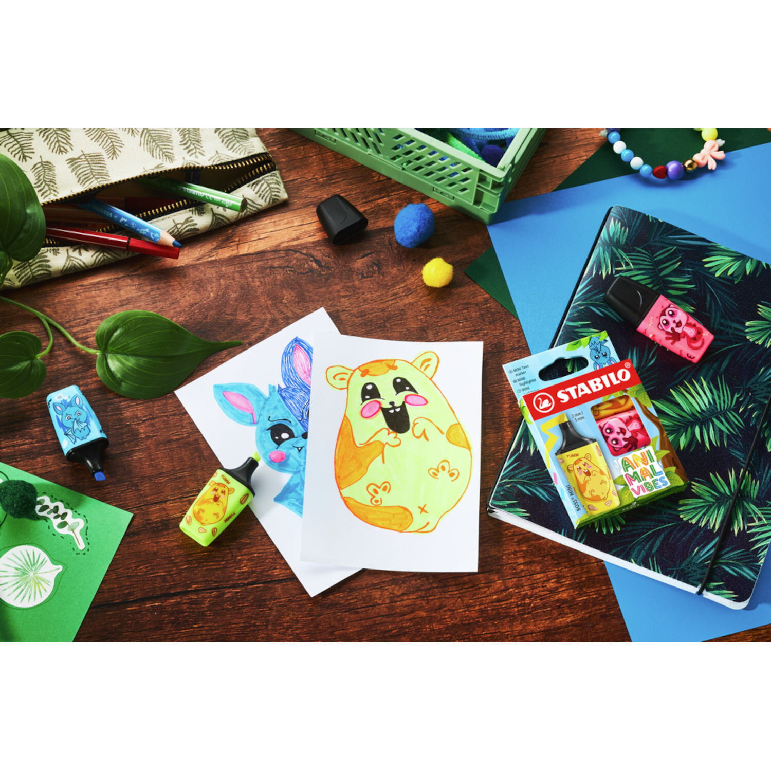 STABILO Boss Mini Animal Vibes Set 3 Stück auf Holztisch mit farbigen Tierzeichnungen, tropisch gemustertem Notizbuch und kreativem Schulzubehör