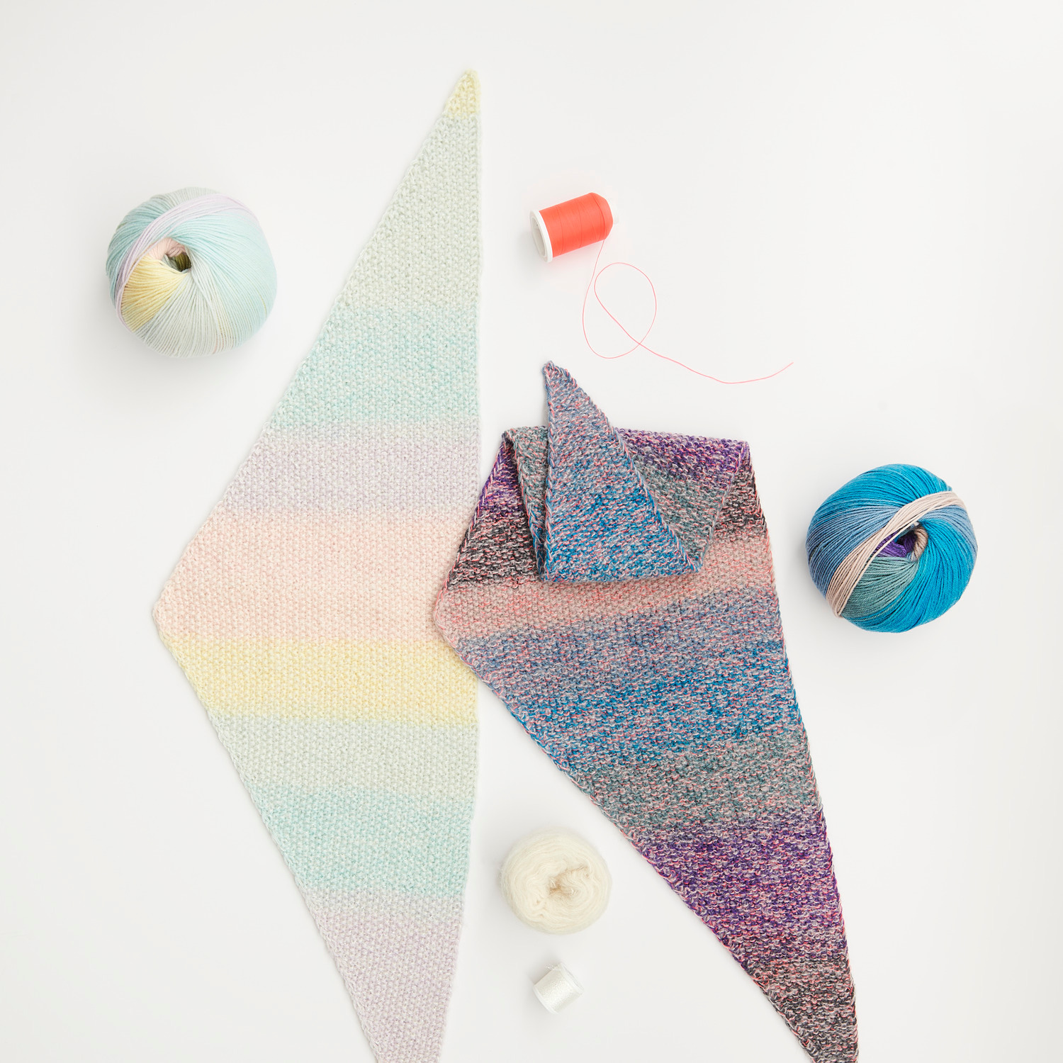 Mini Tücher Special: Zwei gestrickte Tücher in Pastell- und Blautönen, umgeben von buntem Garn.