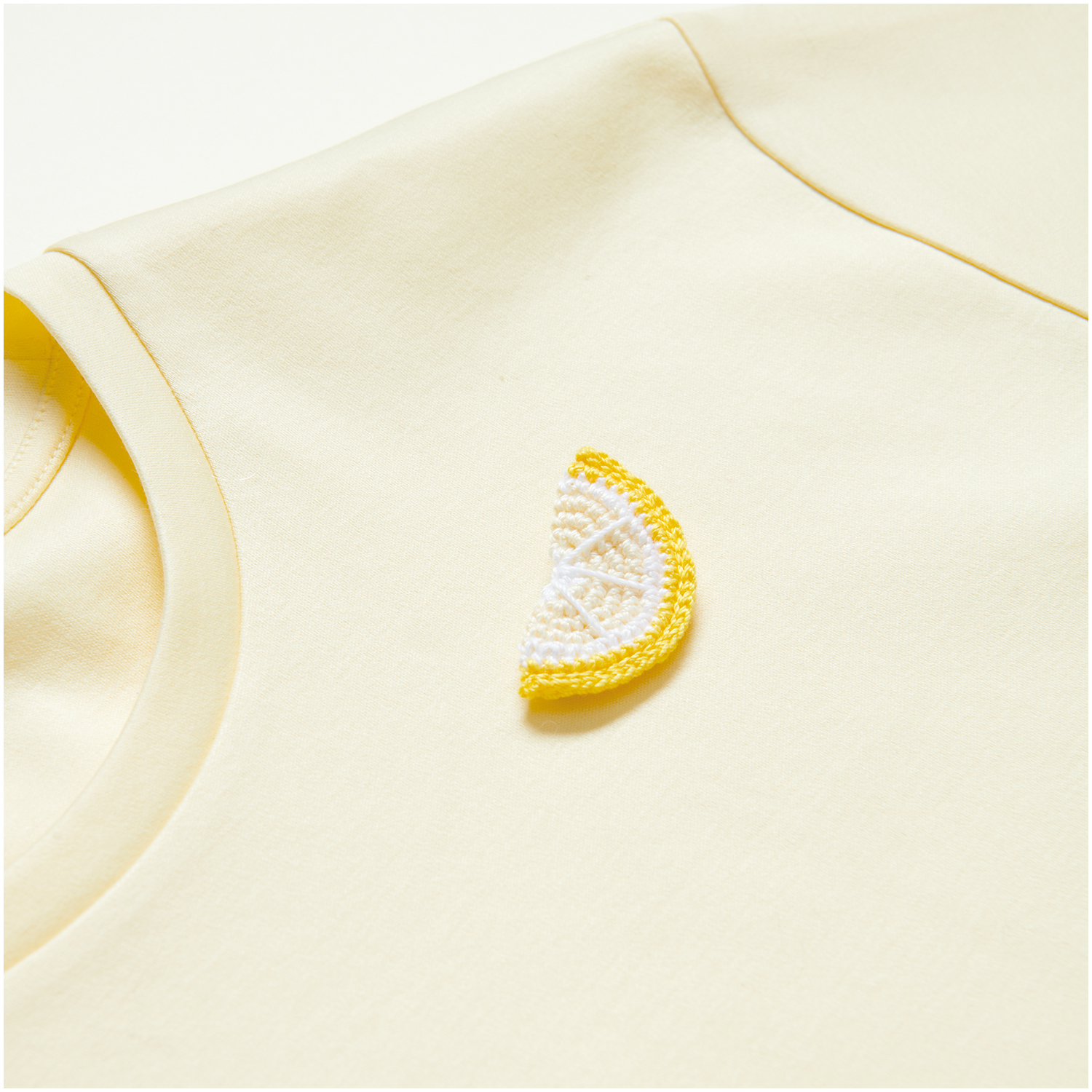 Essentials Crochet: Ein weißes, gehäkeltes Zitronenmotiv auf einem hellgelben T-Shirt von Rico Design.