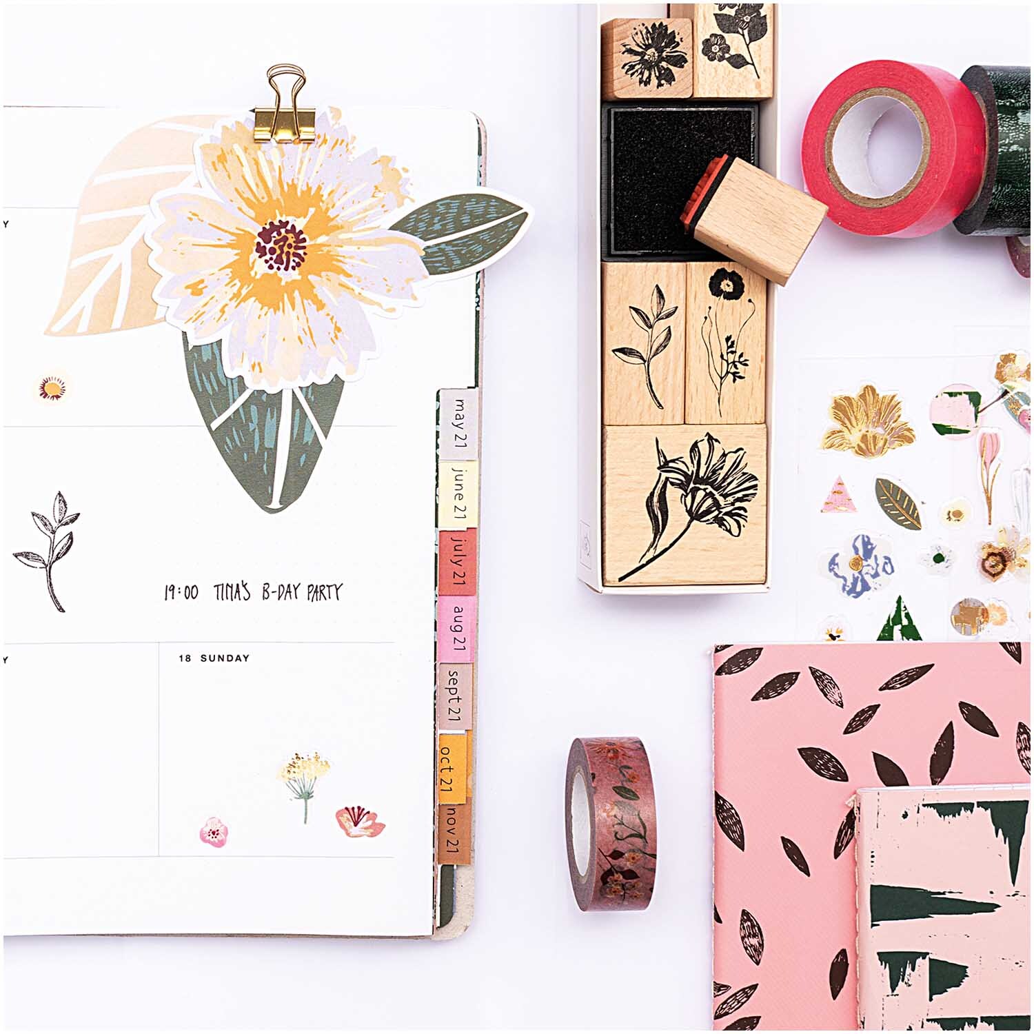 Paper Poetry Papieranhänger Blüten 8 Stück, dekoriert mit floralen Motiven, neben Stempeln und Washi-Tape auf einem Schreibtisch.