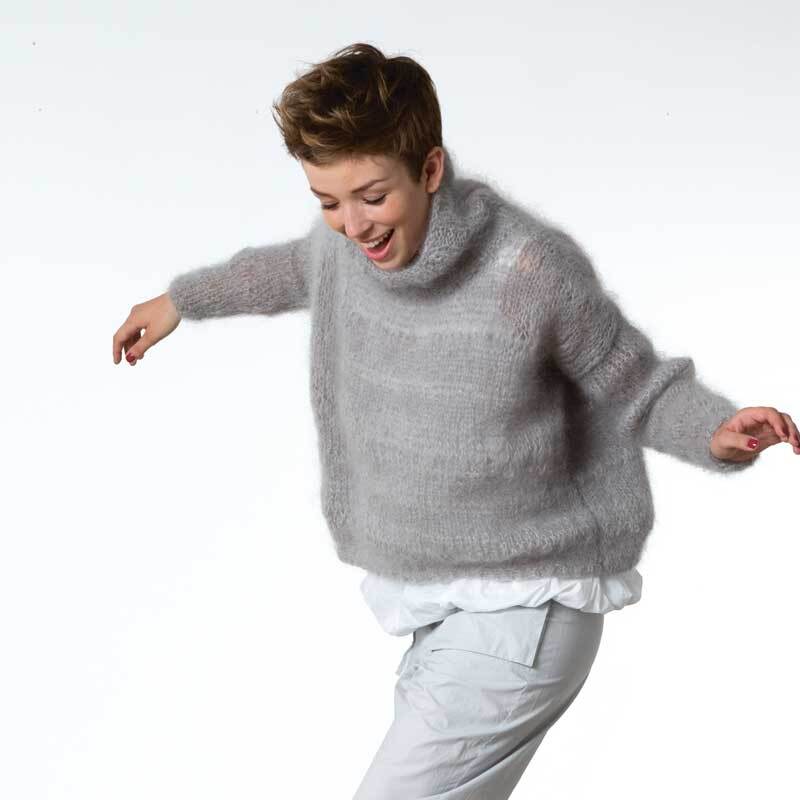 Fashion Glitz Pullover aus weichem Garn von Rico Design. Frau in grauem Strickpullover, lächelnd und in Bewegung.