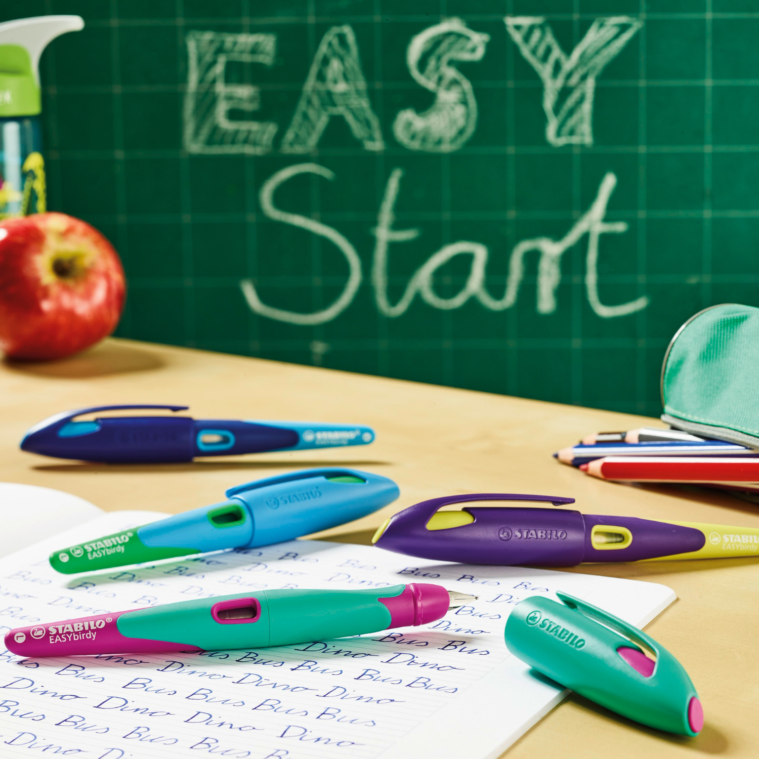 Easybird Patronenfüller für Linkshänder in verschiedenen Farben auf einem Schreibtisch, umgeben von Schulmaterialien.