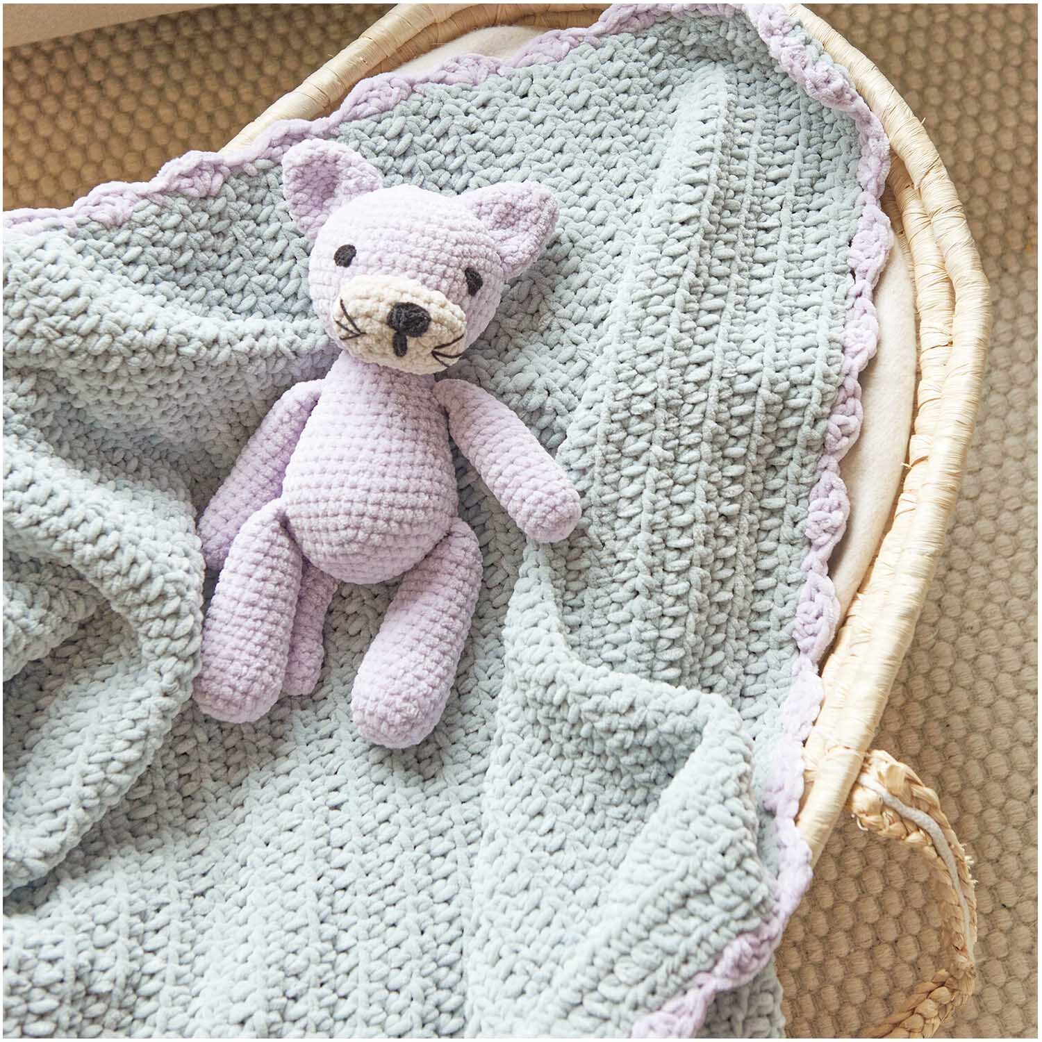 Häkelset Decke Modell 06 aus Baby Chenillove: Weiche, hellblaue Decke mit gehäkeltem, lila Stofftier in einem Korb.