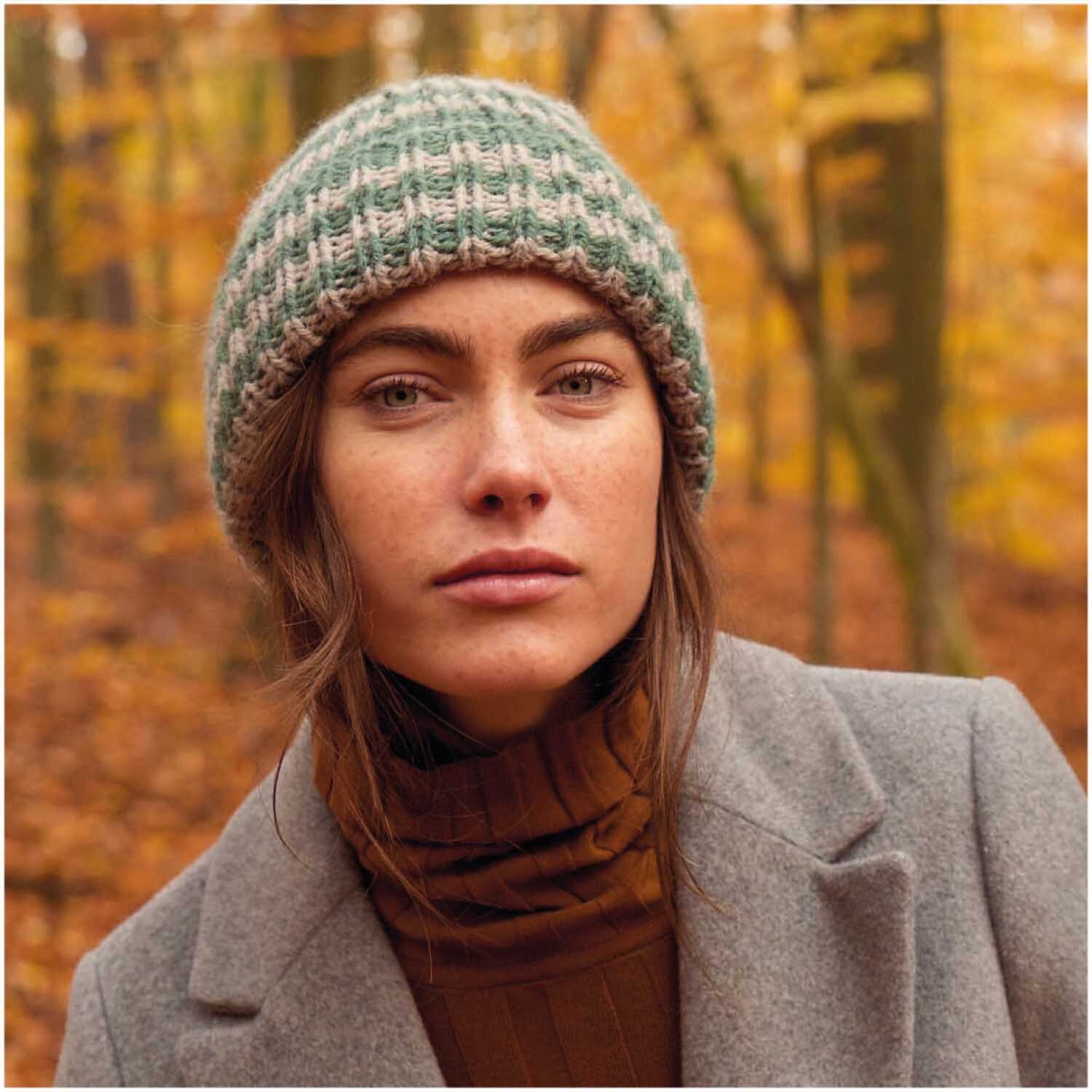 Essentials Alpaca Twist Chunky: Frau mit gestrickter Mütze im Wald, umgeben von herbstlichen Bäumen.