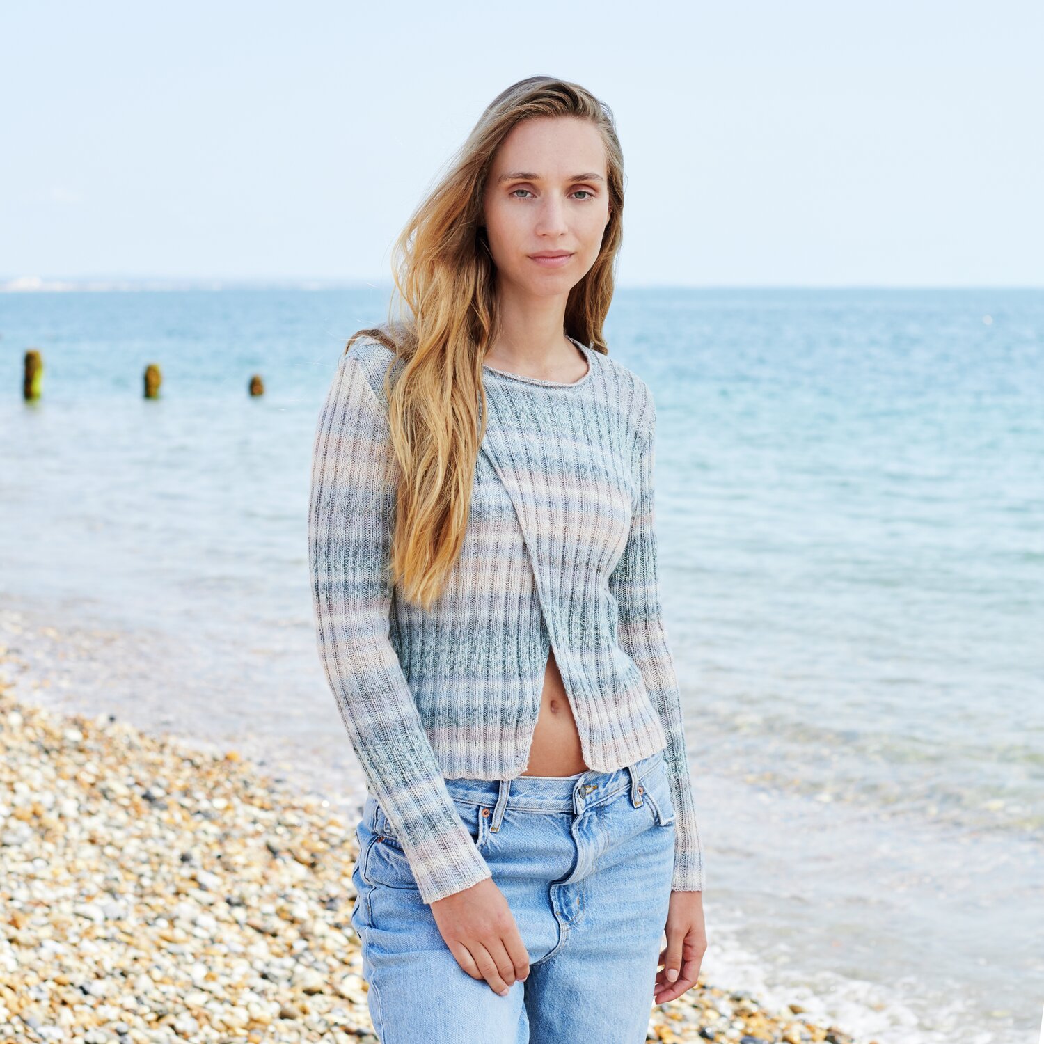 Strickset Pullover Modell 32 aus Lovewool No. 22: Frau am Strand in gestreiftem Pullover und Jeans.