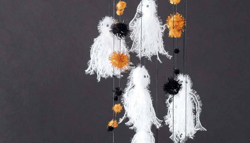 Bastelanleitung Gespenstermobile mit Pompons: Weiße Gespenster und bunte Pompons hängen an Fäden vor schwarzem Hintergrund.