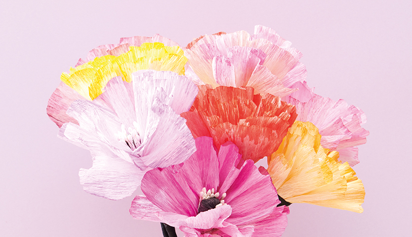 Bastelanleitung DIY-Papierblumen: Bunte Papierblumen in Rosa, Gelb und Orange auf hellem Hintergrund.