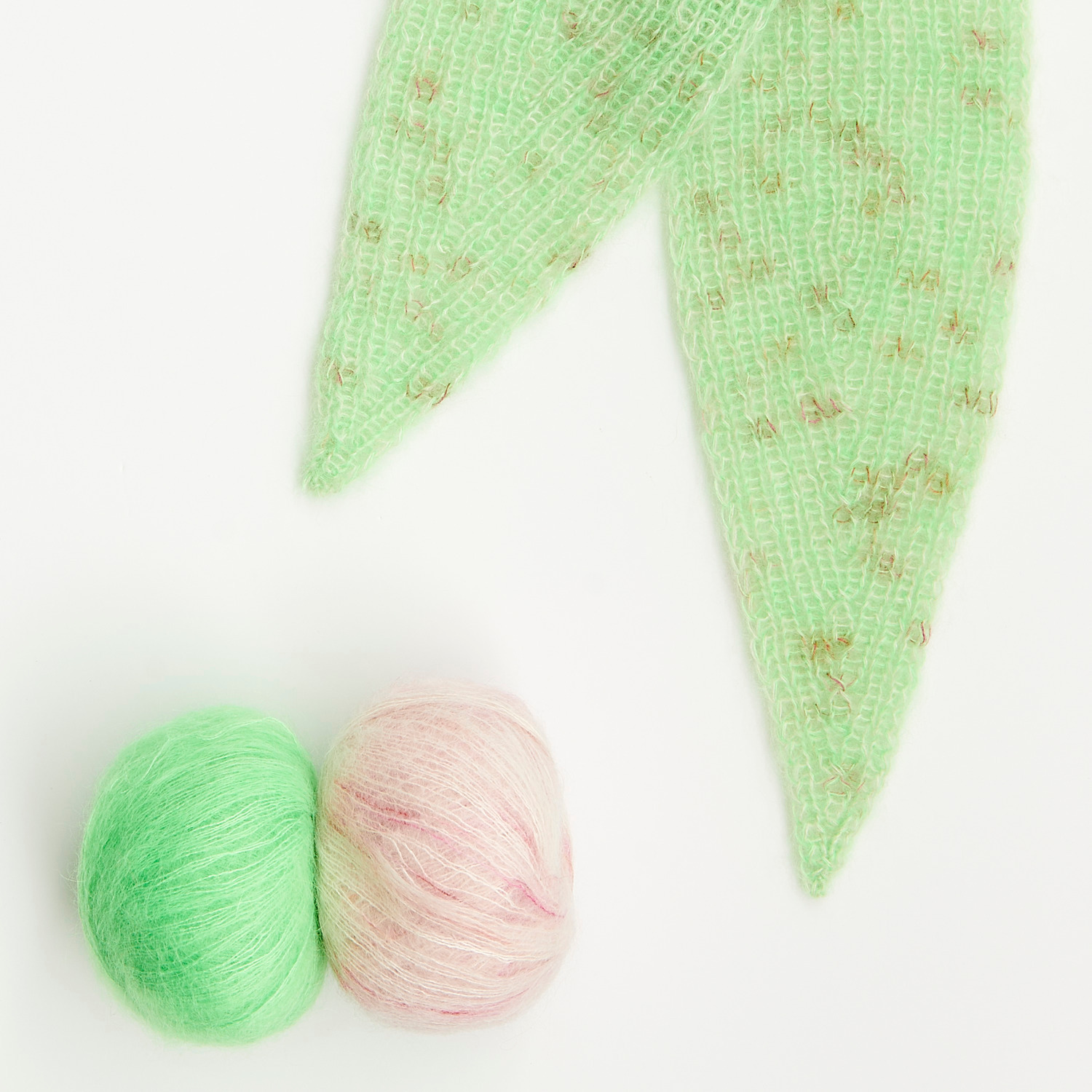 Mini Tücher Special von Rico Design: Zwei Wollknäuel in Grün und Rosa neben einem gestrickten Tuch.