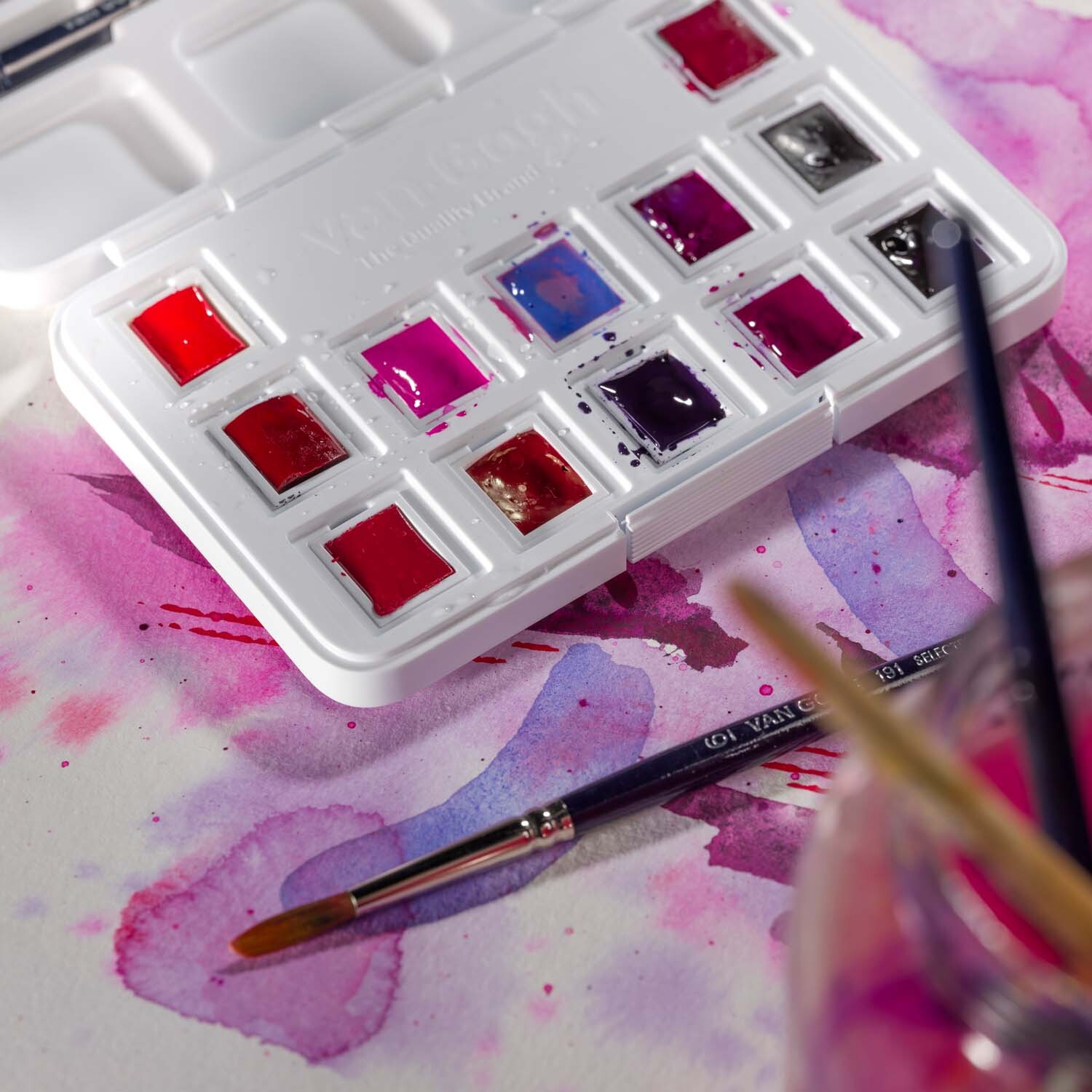 Aquarell Set Rosa-Violett 12 Näpfchen von van Gogh auf einem gemusterten Hintergrund mit Pinseln.