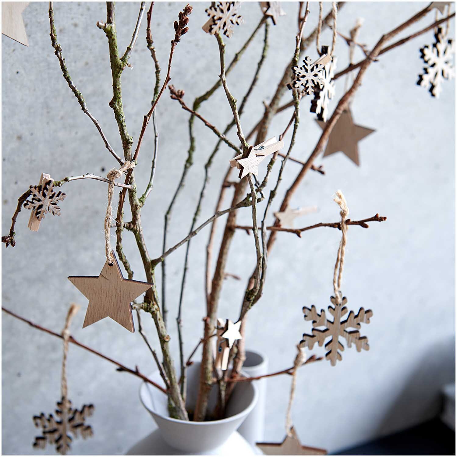 Holzhänger Stern natur 51x50mm 3 Stück: Dekorative Holzsterne an Zweigen in einer Vase, ideal für natürliche Weihnachtsdekoration.
