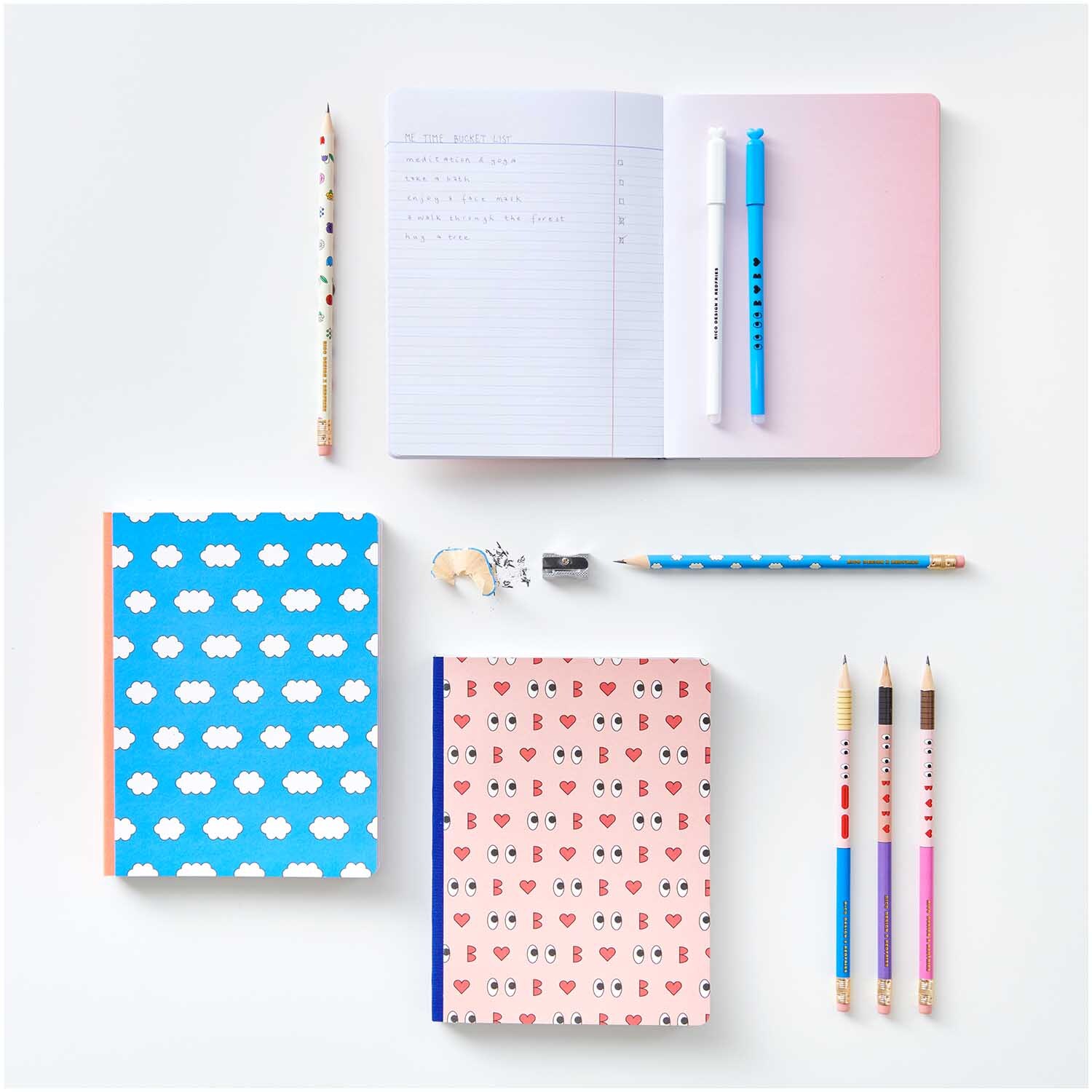 Rico Design x Redfries Notizbuch Wolken mit blauem Cover, umgeben von Stiften und weiteren Notizbüchern auf einem Tisch.