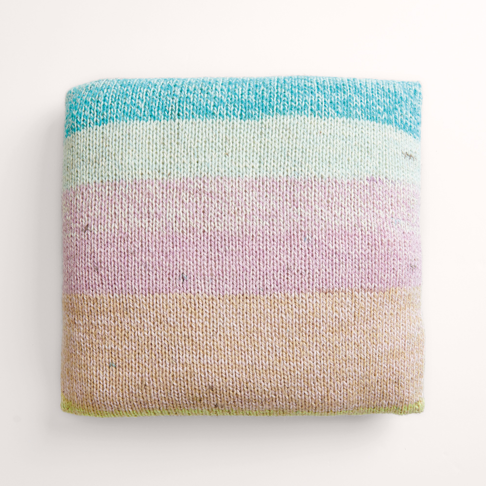 Buntes Kissen auf grauem Hintergrund – zum Strickset