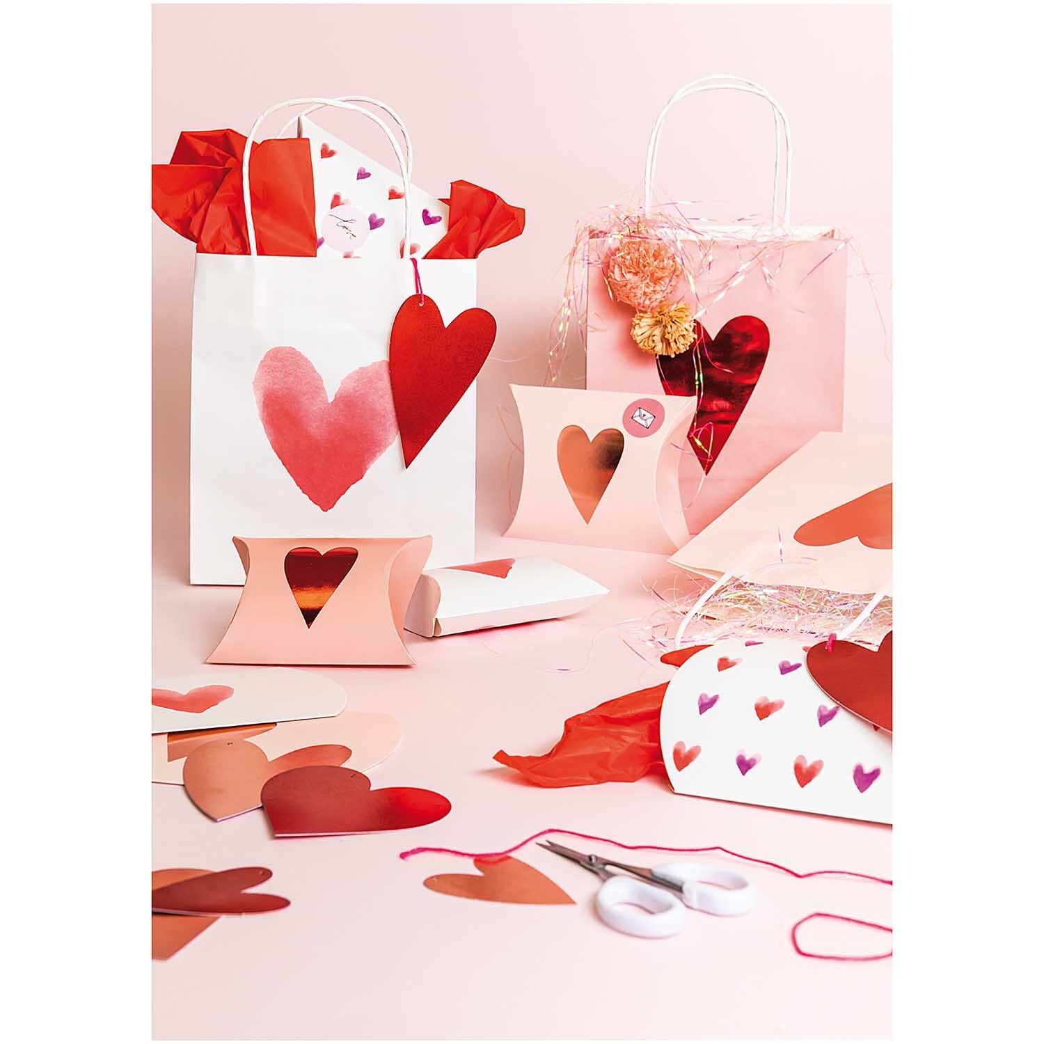 Paper Poetry Papiertüten It must be love: Geschenkverpackungen mit Herzmotiven in Aquarelloptik, dekoriert mit roten und rosa Akzenten.