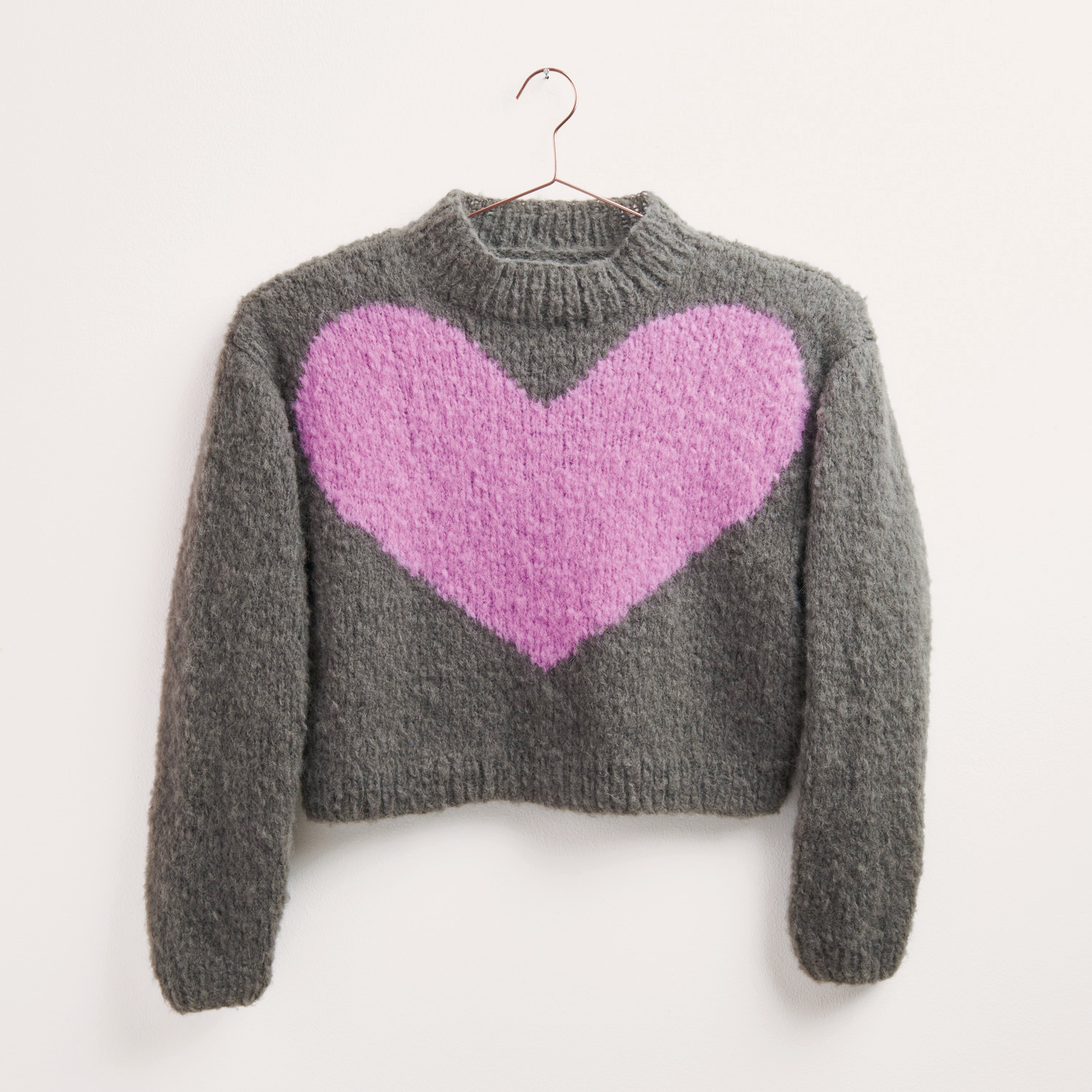 Strickset Pullover Modell 34 zeigt einen grauen Pullover mit großem rosa Herzmotiv, ideal für Herbst-Winter. Marke: Rico Design.