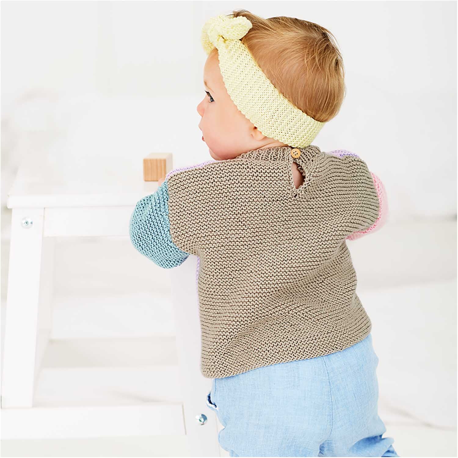 Rico Baby Cotton Soft dk: Ein Baby trägt einen gestrickten Pullover in sanften Farben, passend zu einer hellen Umgebung.