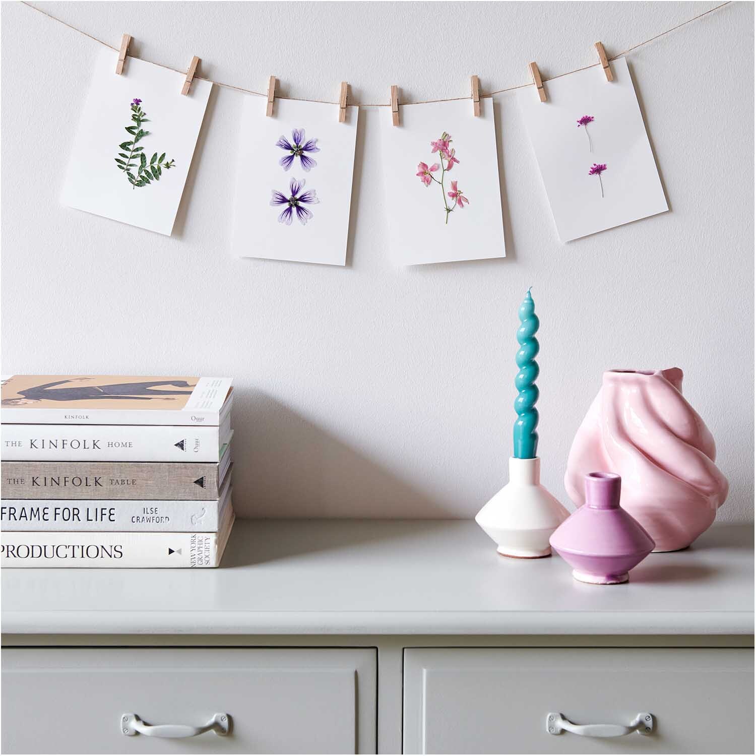 Gepresste Blüten Ammi pink 6 Stück von Rico Design, dekorativ auf Karten an einer Leine über einem Tisch mit Vasen und Büchern arrangiert.