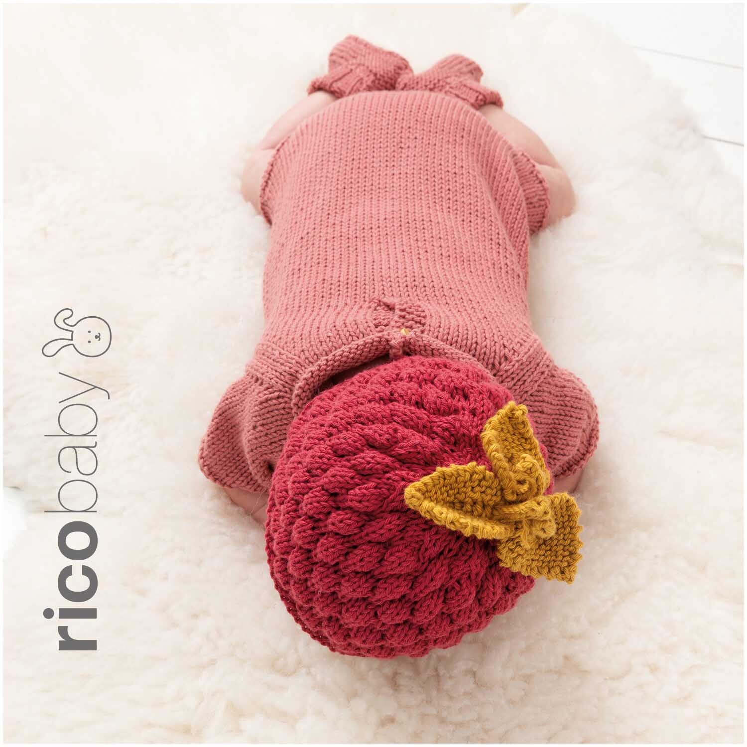 Rico Baby Cotton Soft dk: Ein Baby in himbeerfarbener Strickkleidung mit gelber Schleife auf weicher Decke.