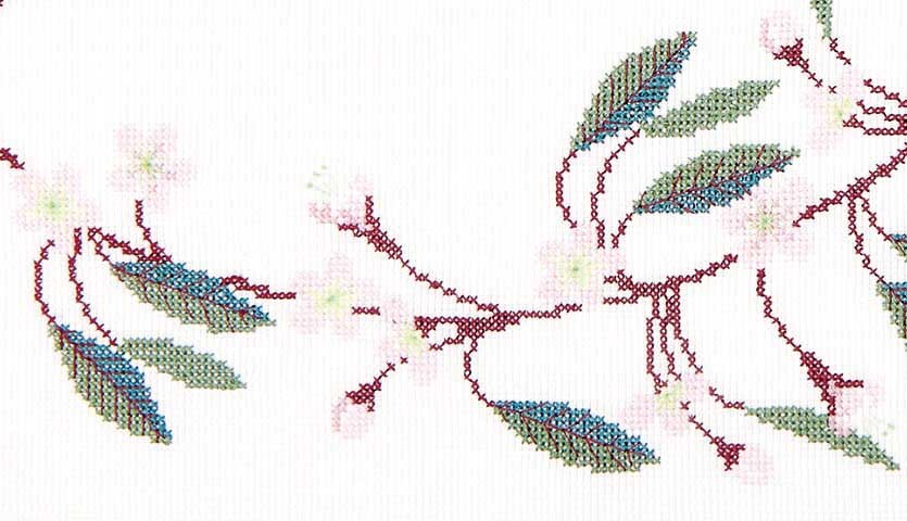 Stickanleitung Tischdecke mit Kirschzweigen: Filigrane Kirschzweige in Rot und Grün auf weißem Stoff.