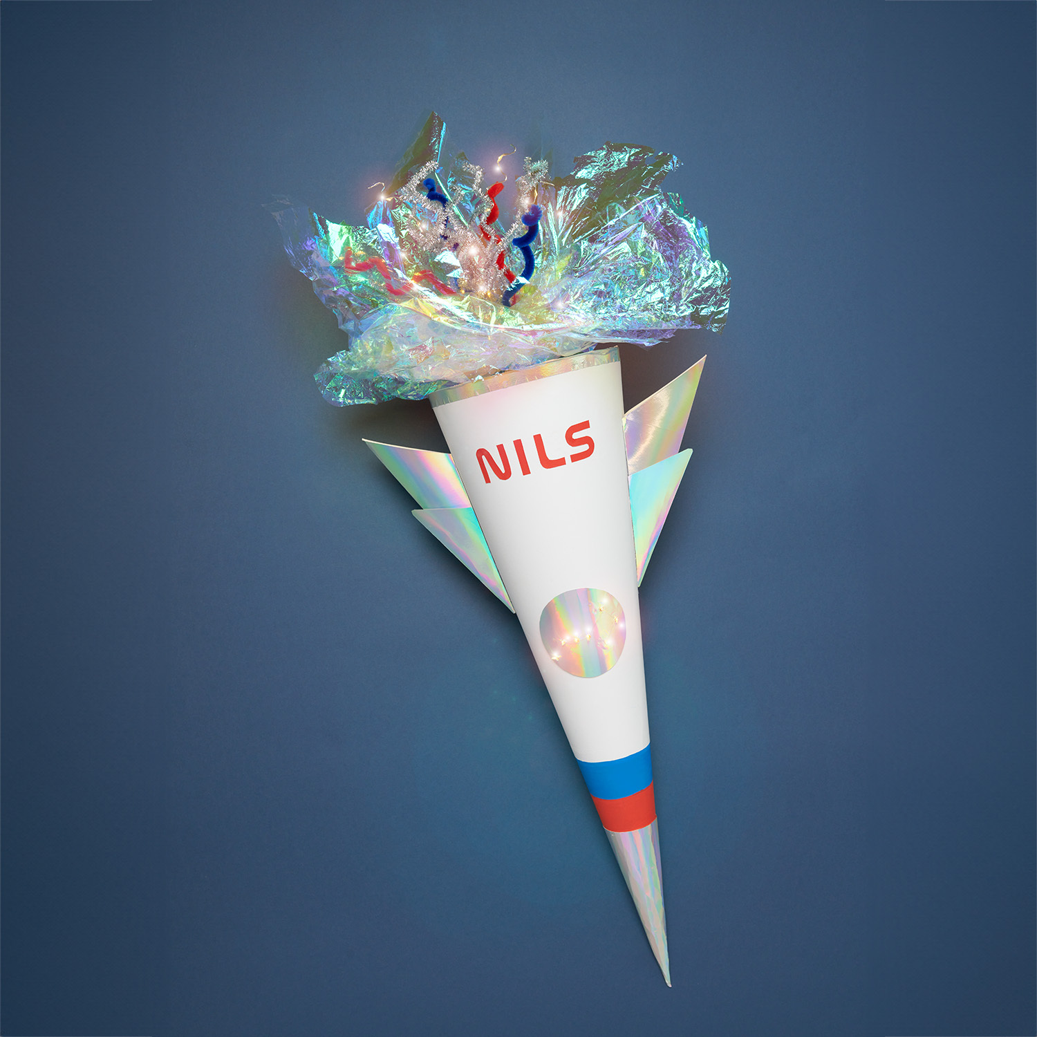 Bastelset Schultüte Rakete: Weiße Schultüte in Raketenform mit buntem Dekor von Rico Design auf blauem Hintergrund.