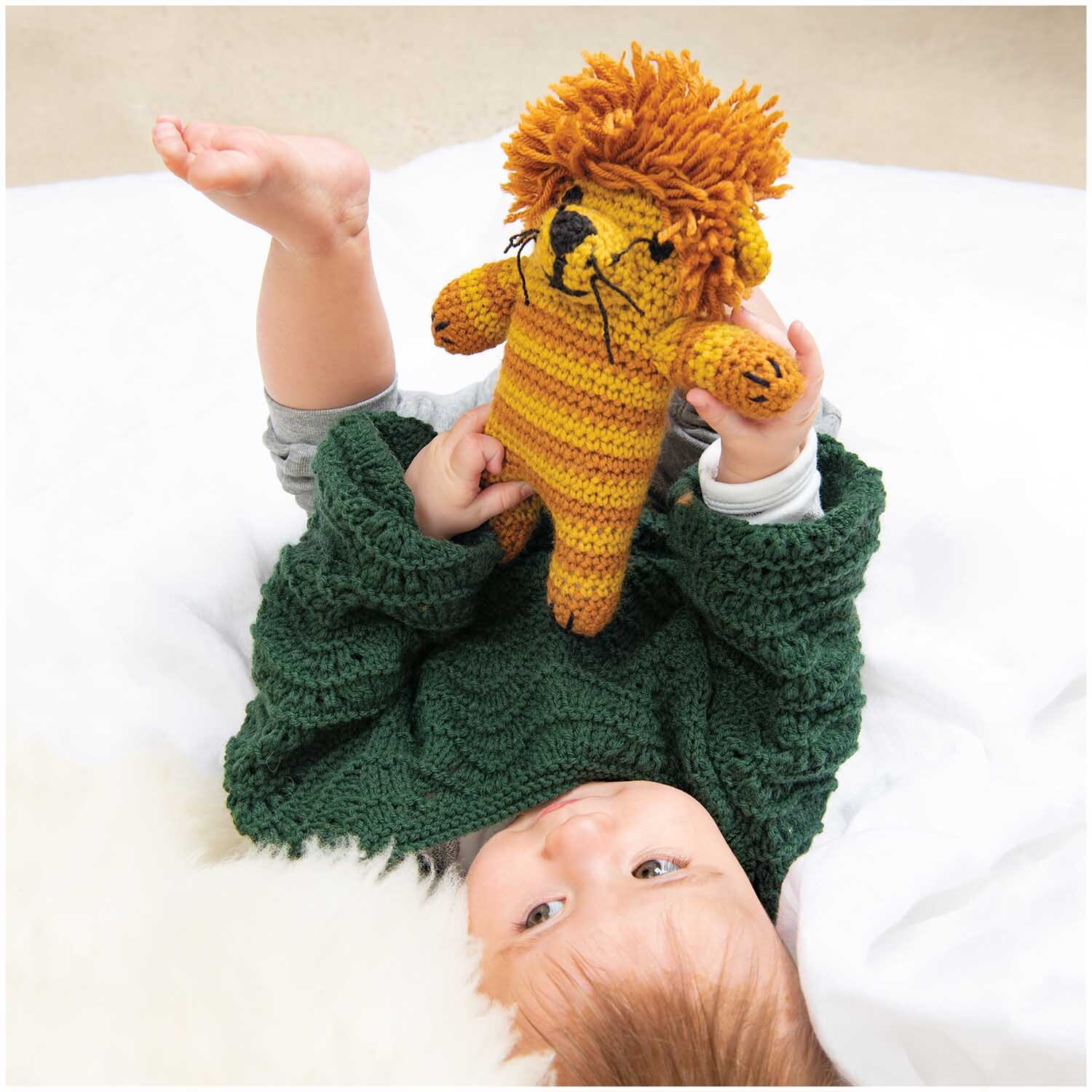 Rico Baby Classic dk: Ein Baby spielt mit einem gestrickten Löwen in Senf, umhüllt von einer grünen Decke.