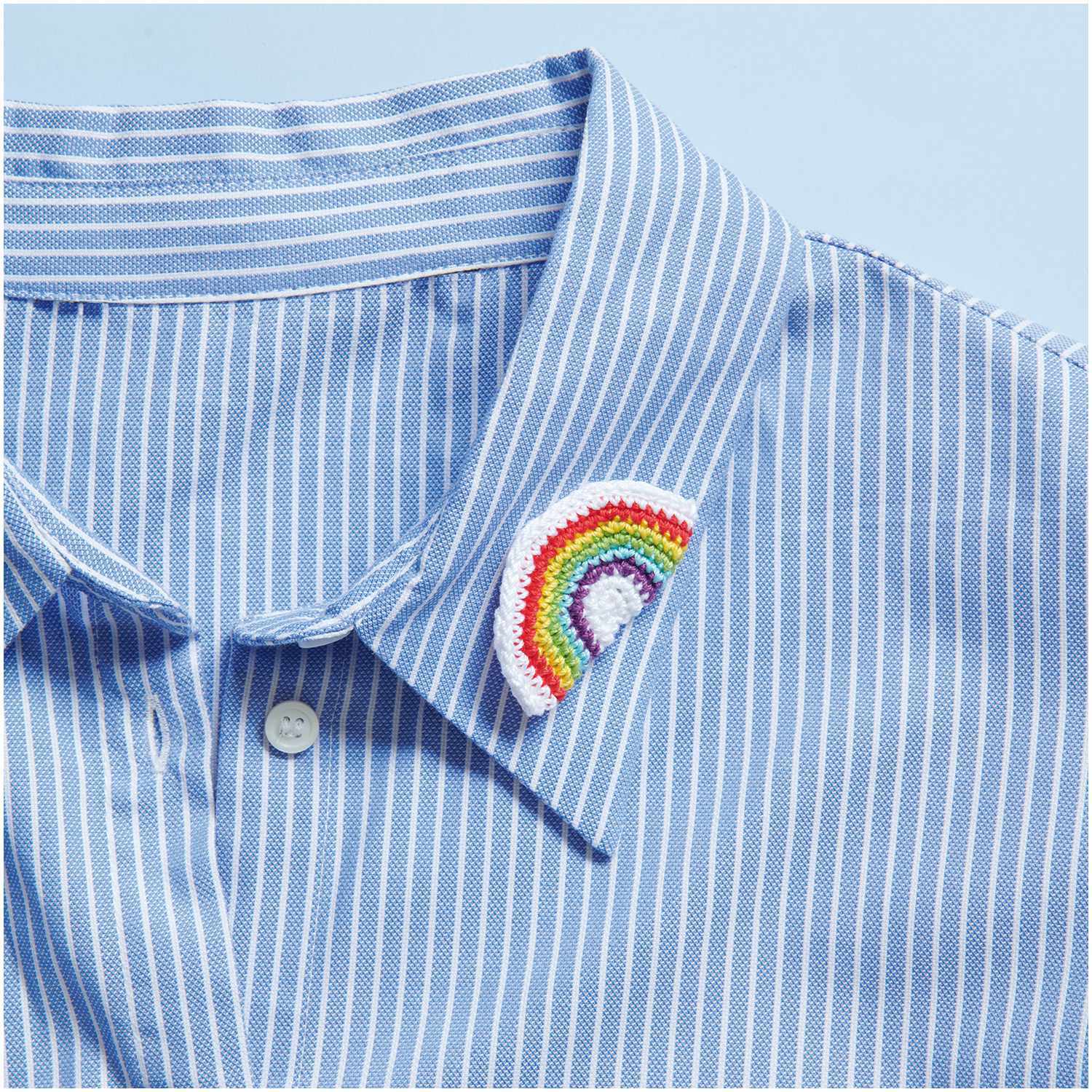 Essentials Crochet: Ein gestreiftes Hemd mit einem gehäkelten Regenbogen-Emblem am Kragen. Ideal für kreative Designs.