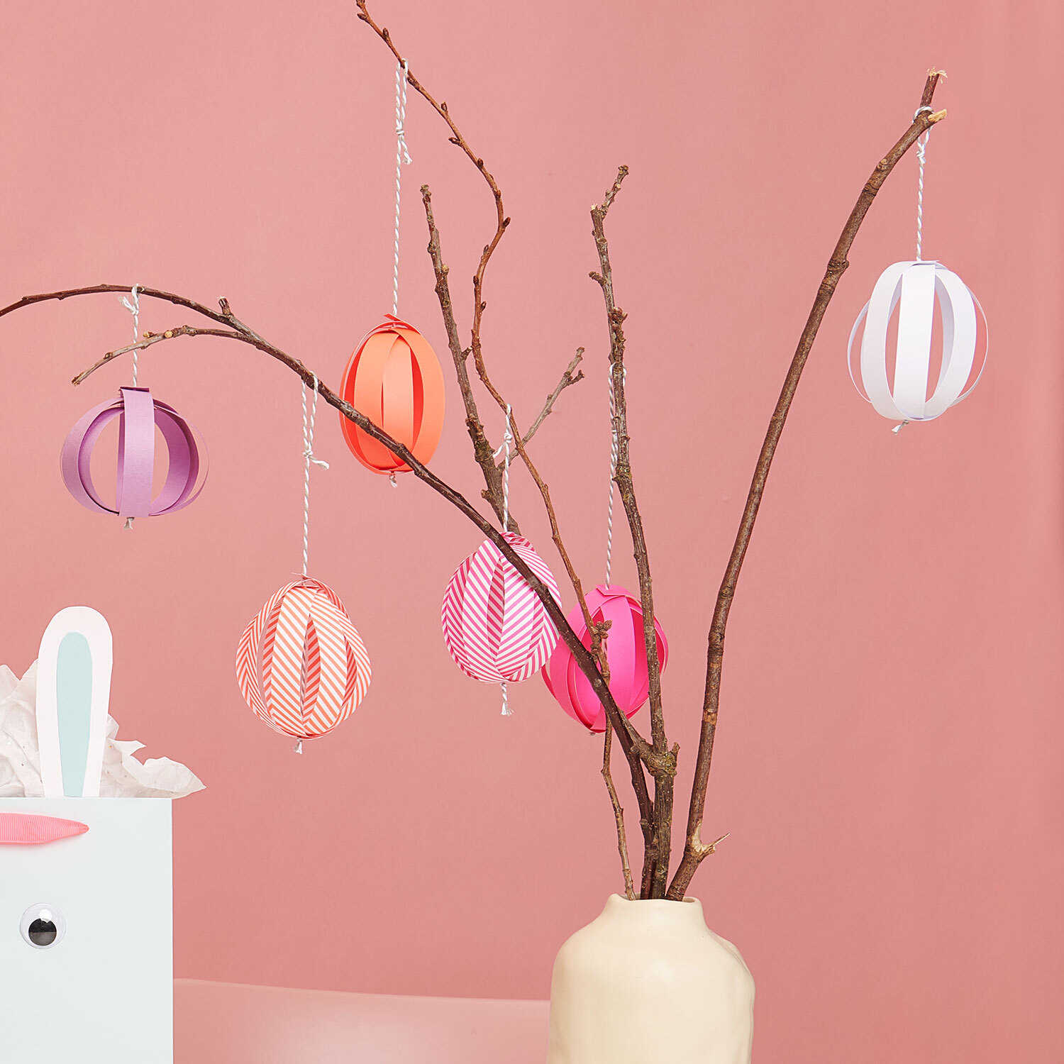 Bastelanleitung Ostereier aus Fröbelstreifen: Bunte Papier-Ostereier hängen an einem dekorativen Zweig in einer Vase.