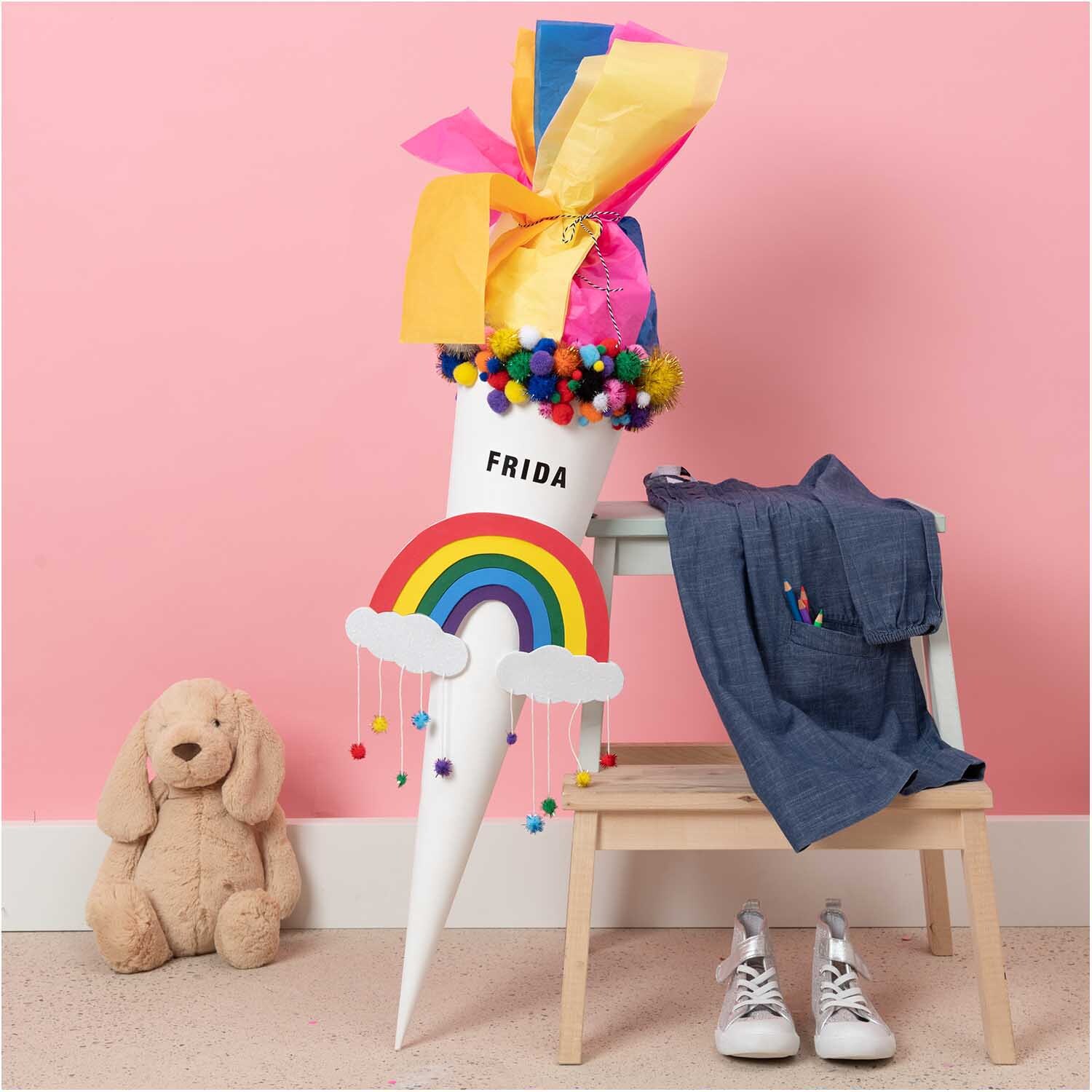 Paper Poetry Schultüte Rohling, dekoriert mit buntem Papier und Pompons, steht neben einem Stuhl mit Kleidung und einem Plüschtier.