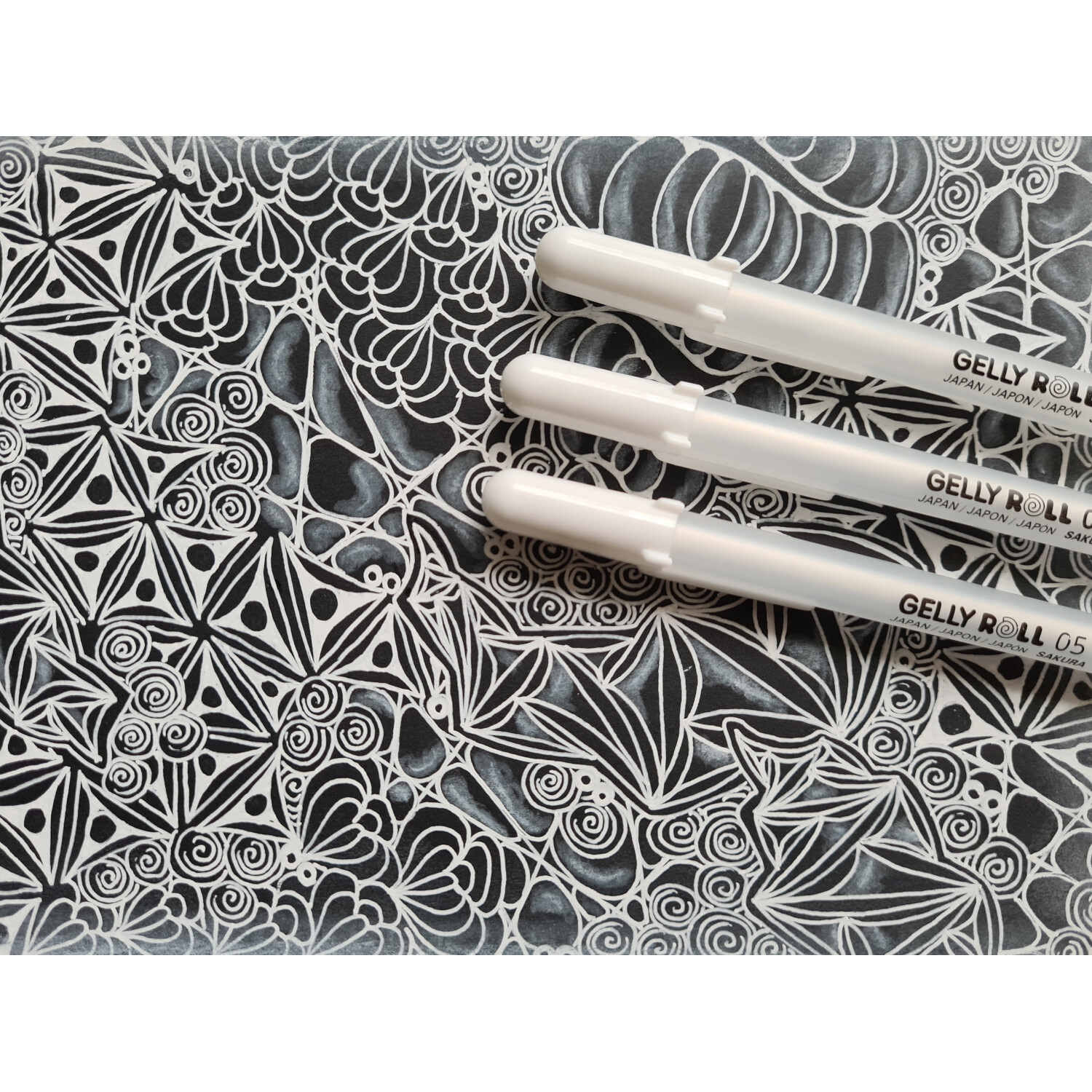 Gelly Roll Gelstifte Basic-Set Bright White auf detailliertem, schwarzem Musterhintergrund. Ideal für kreative Zeichnungen.