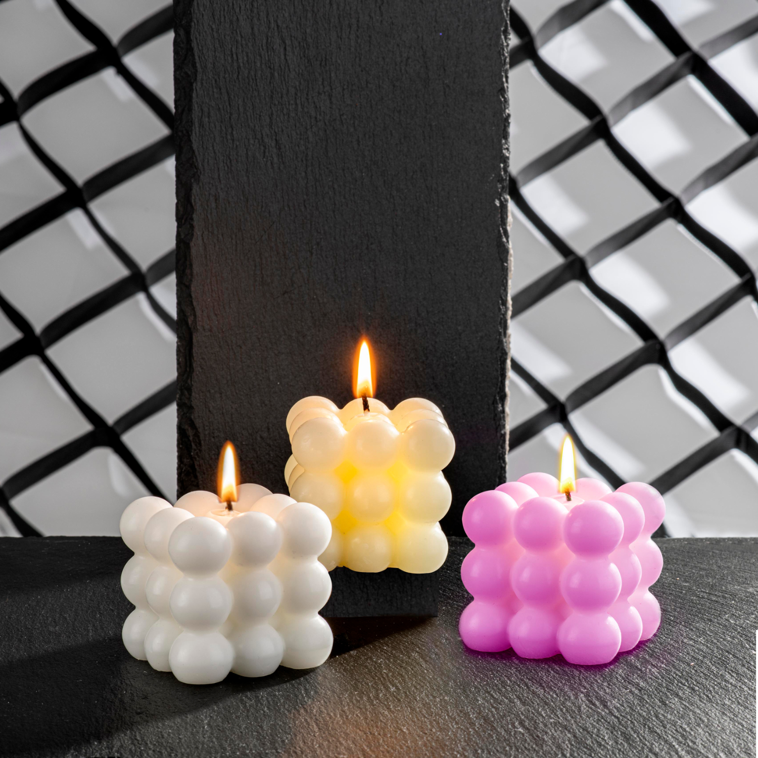 Kerzengießform Bubble: Drei brennende Kerzen in Weiß, Gelb und Rosa auf schwarzem Hintergrund.