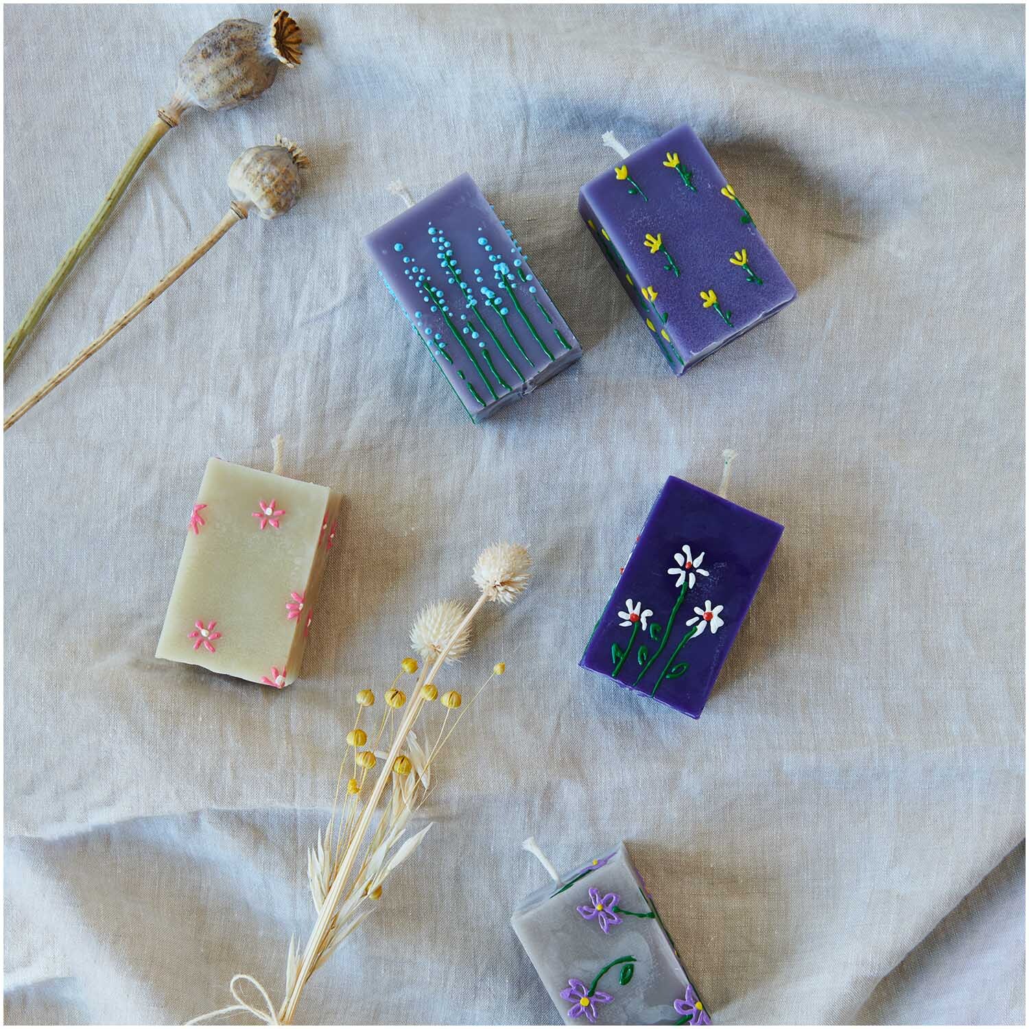 Candle Liner Kerzenmalfarbe Set Regenbogen: Fünf dekorierte Kerzen auf Leinentuch, verziert mit floralen Mustern in verschiedenen Farben.