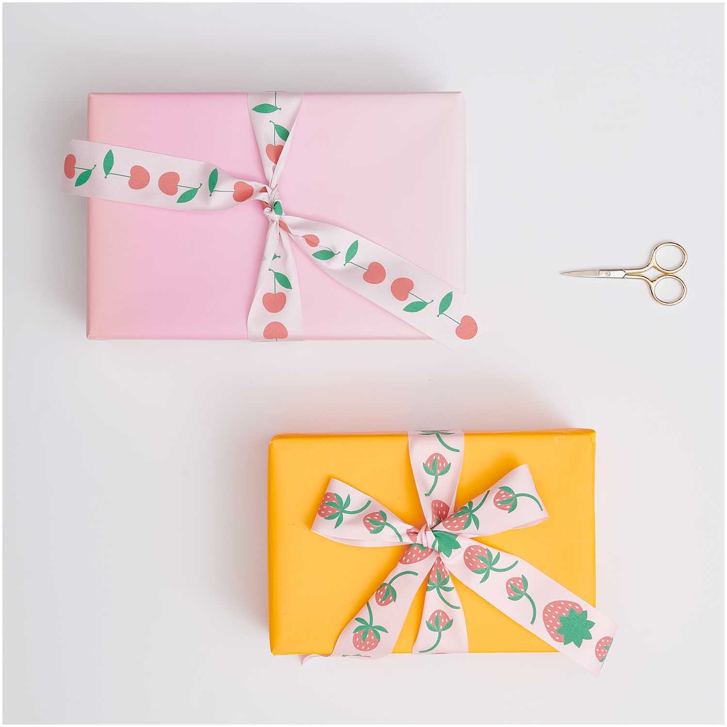Paper Poetry Taftband Kirschen verziert rosa und gelbe Geschenke, begleitet von einer Schere. Ideal für kreative Verpackungen.