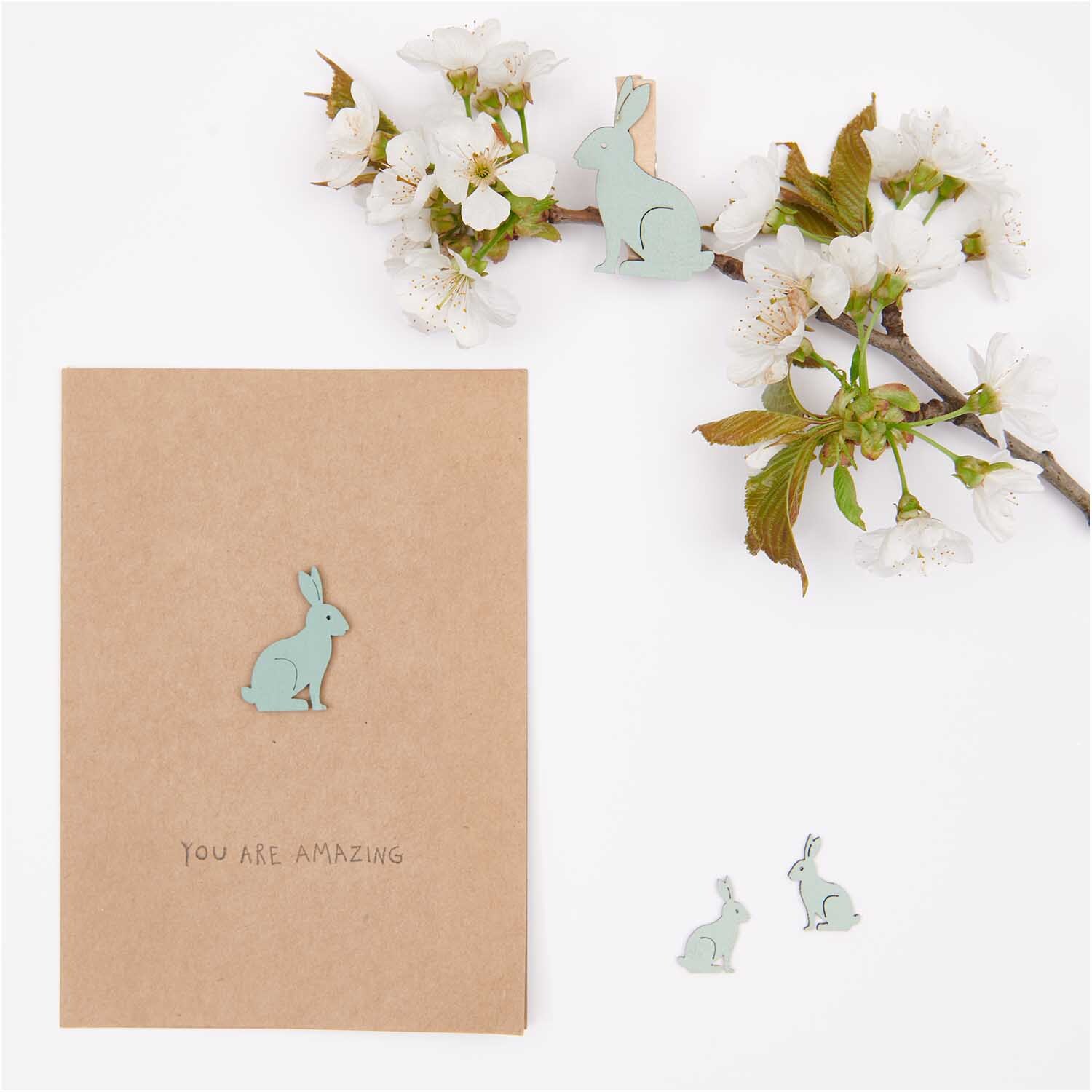 Holzstreu Hase klein 48 Stück: Dekorative Hasen in Mint neben einer Karte und Kirschblüten.