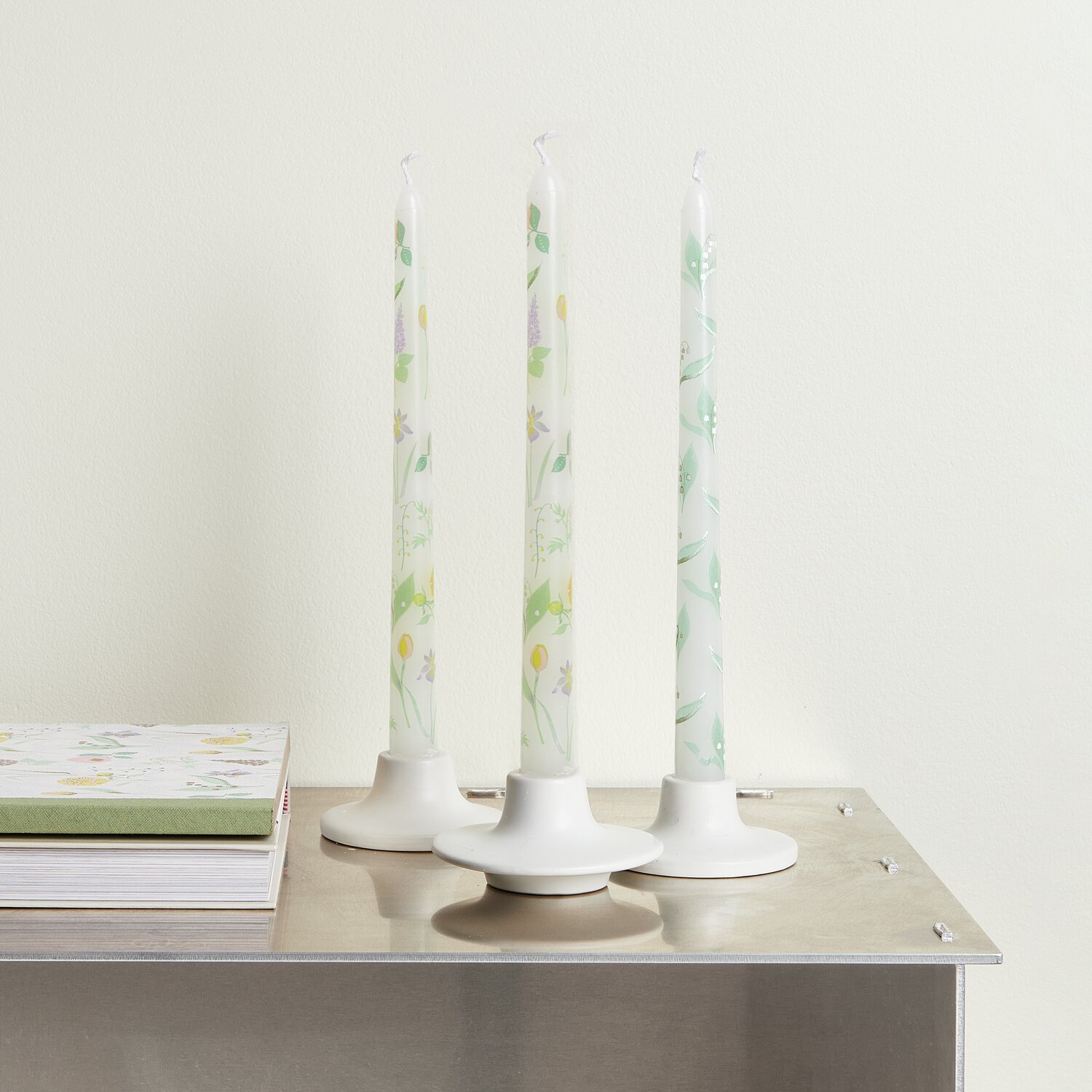 Spitzkerze Maiglöckchen 2 Stück, dekorative weiße Kerzen mit Frühlingsblumenmotiv auf Metalltisch.