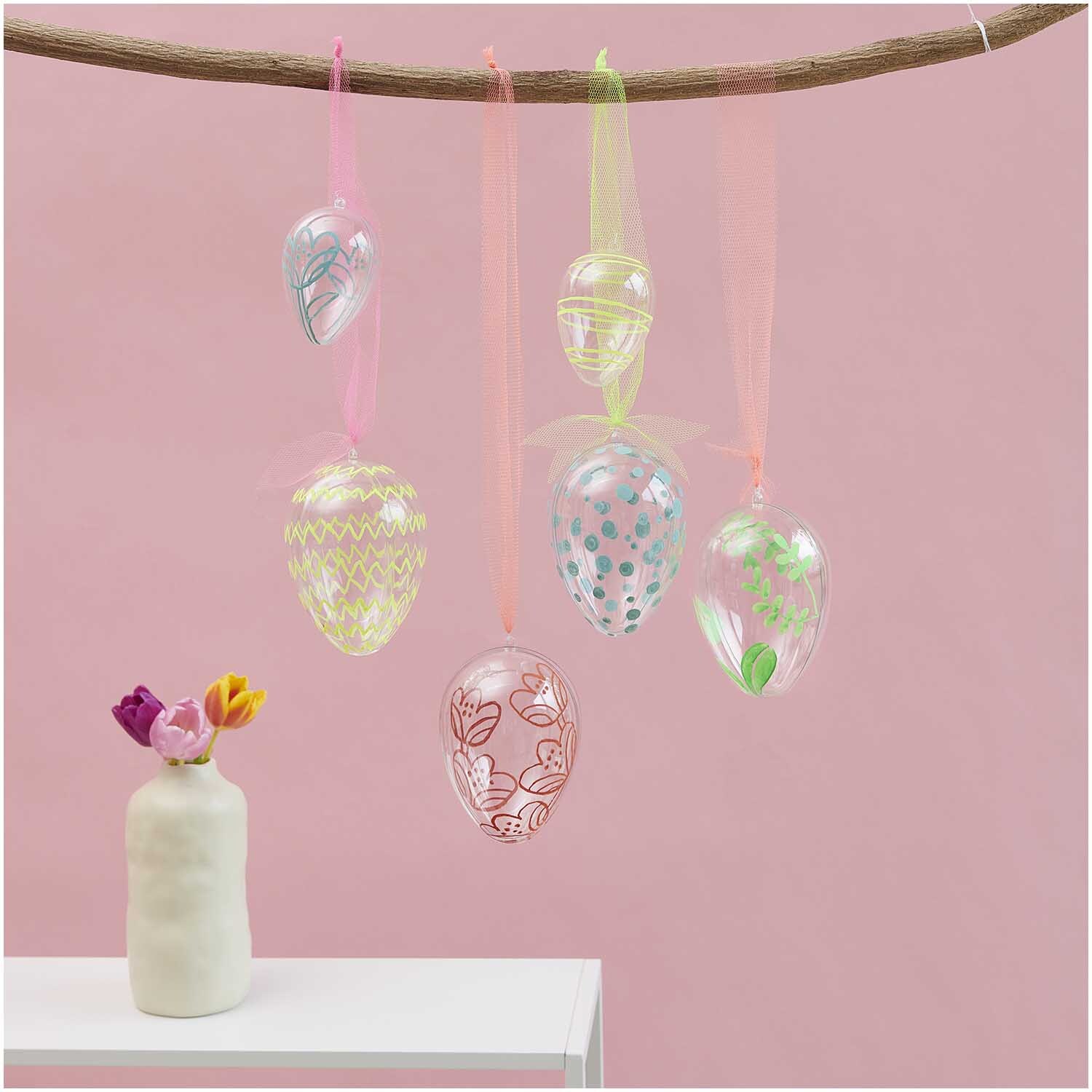 Glas Eier transparent 4 Stück Ø 3cm, dekorativ hängend an einem Ast vor rosa Hintergrund.