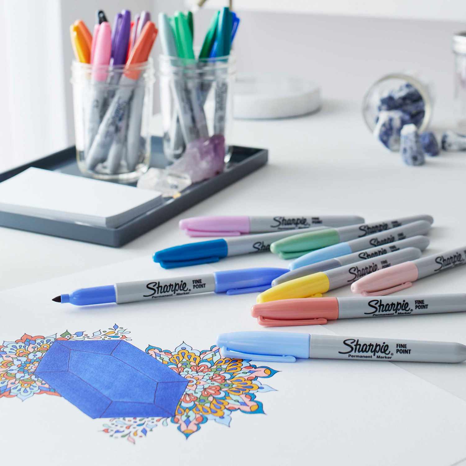 Permanentmarker Mystic Gems 12 Stück von Sharpie auf einem Schreibtisch, umgeben von bunten Zeichnungen und Gläsern mit weiteren Markern.
