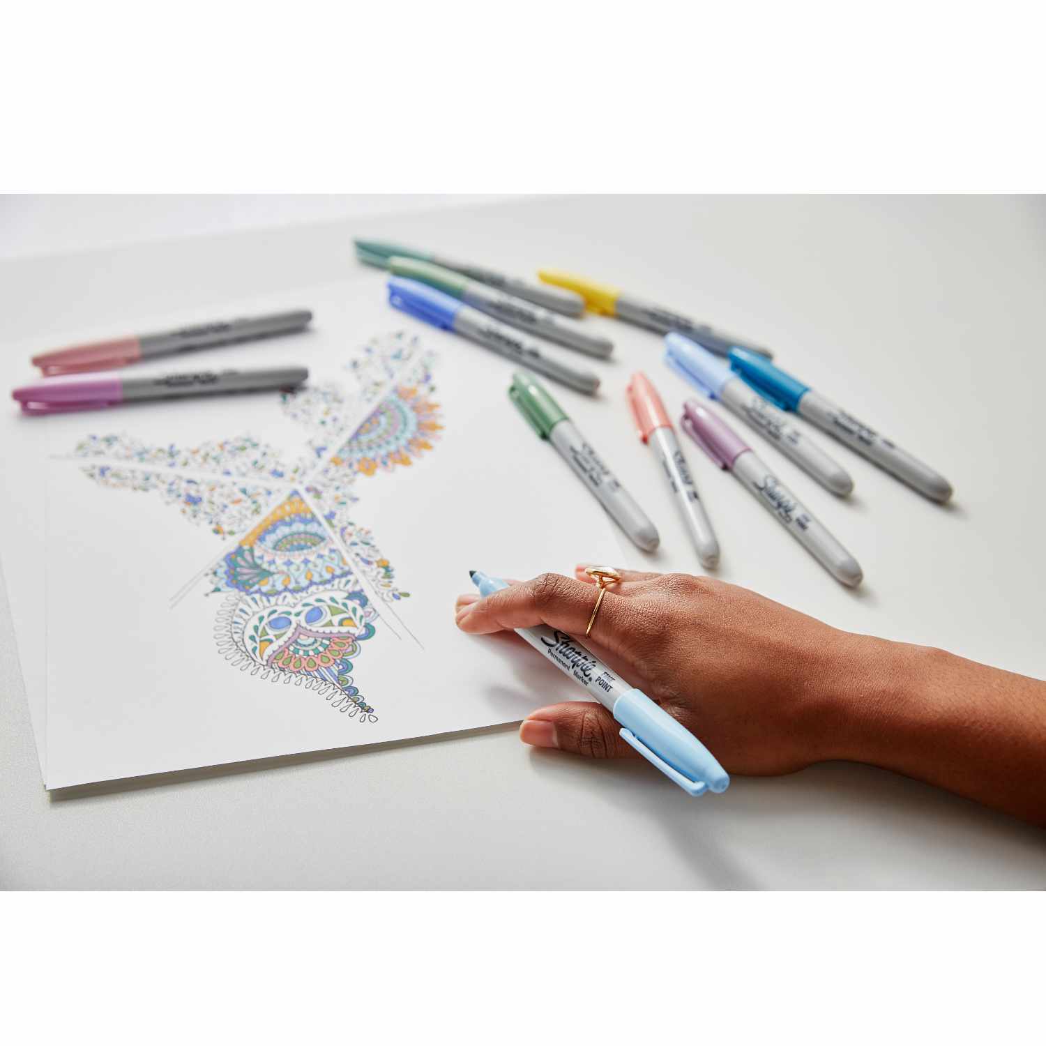 Permanentmarker Mystic Gems 12 Stück: Eine Hand koloriert ein Schmetterlingsbild mit bunten Sharpie-Markern.