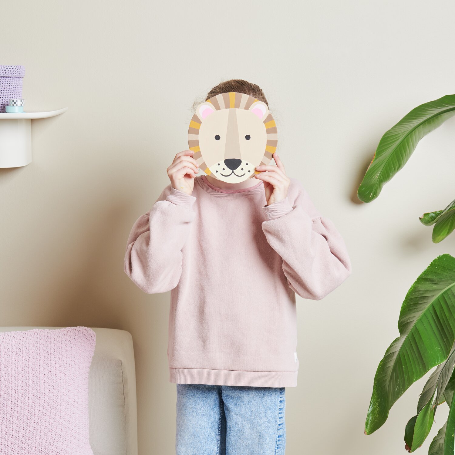 Malen nach Zahlen Löwe: Kind hält ein Löwenbild vor dem Gesicht, trägt rosa Pullover, Rico Design.