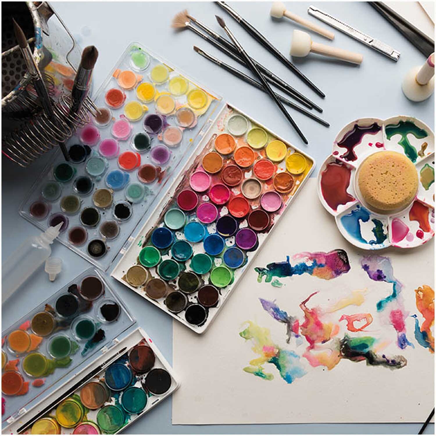 Basic Pearl Water Colours Wasserfarbkasten mit 12 Farben und Pinseln auf einem Tisch arrangiert.