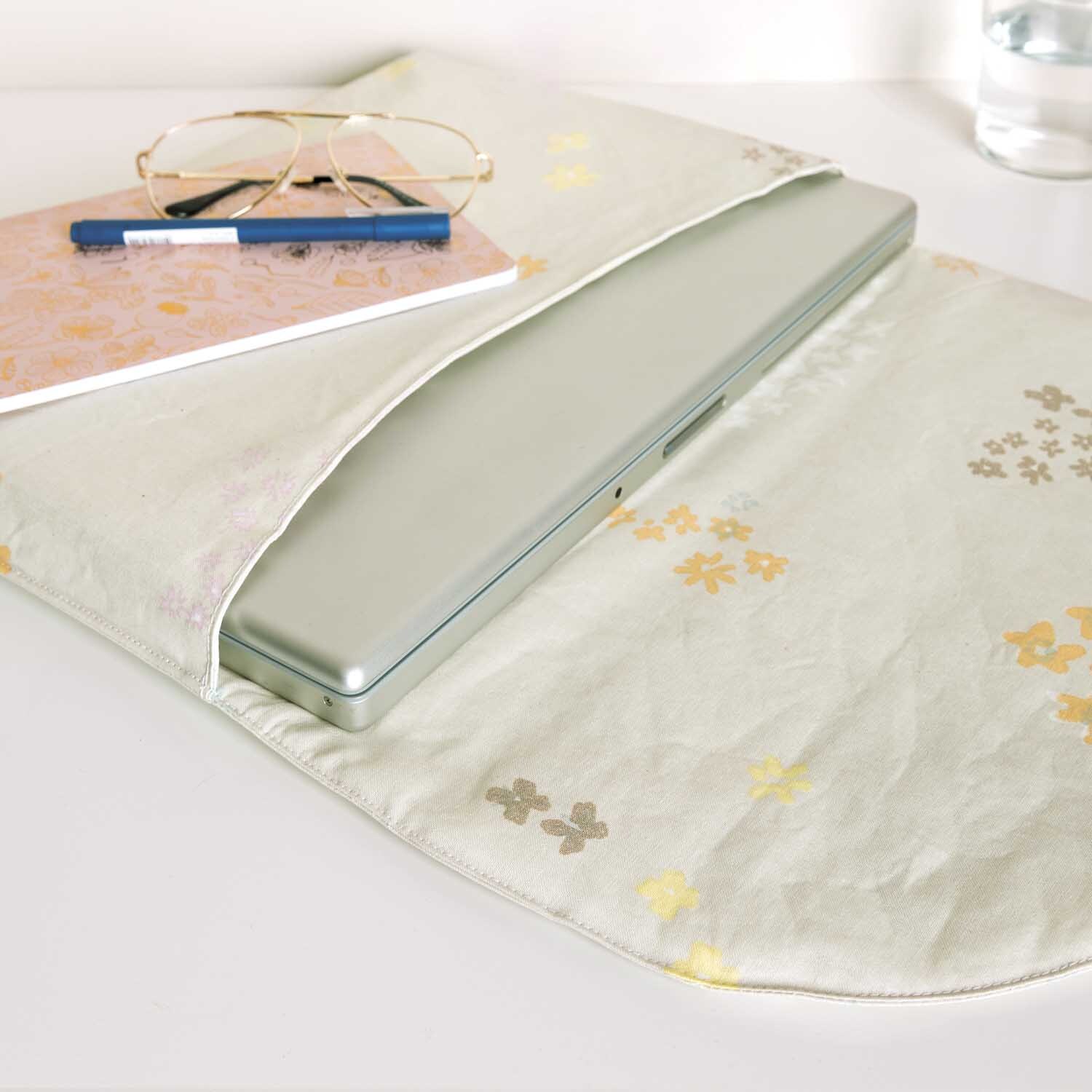 Druckstoff Crafted Nature Blumen grau-metallic von Rico Design, zeigt Laptop-Hülle mit floralen Mustern auf Schreibtisch mit Brille und Notizbuch.