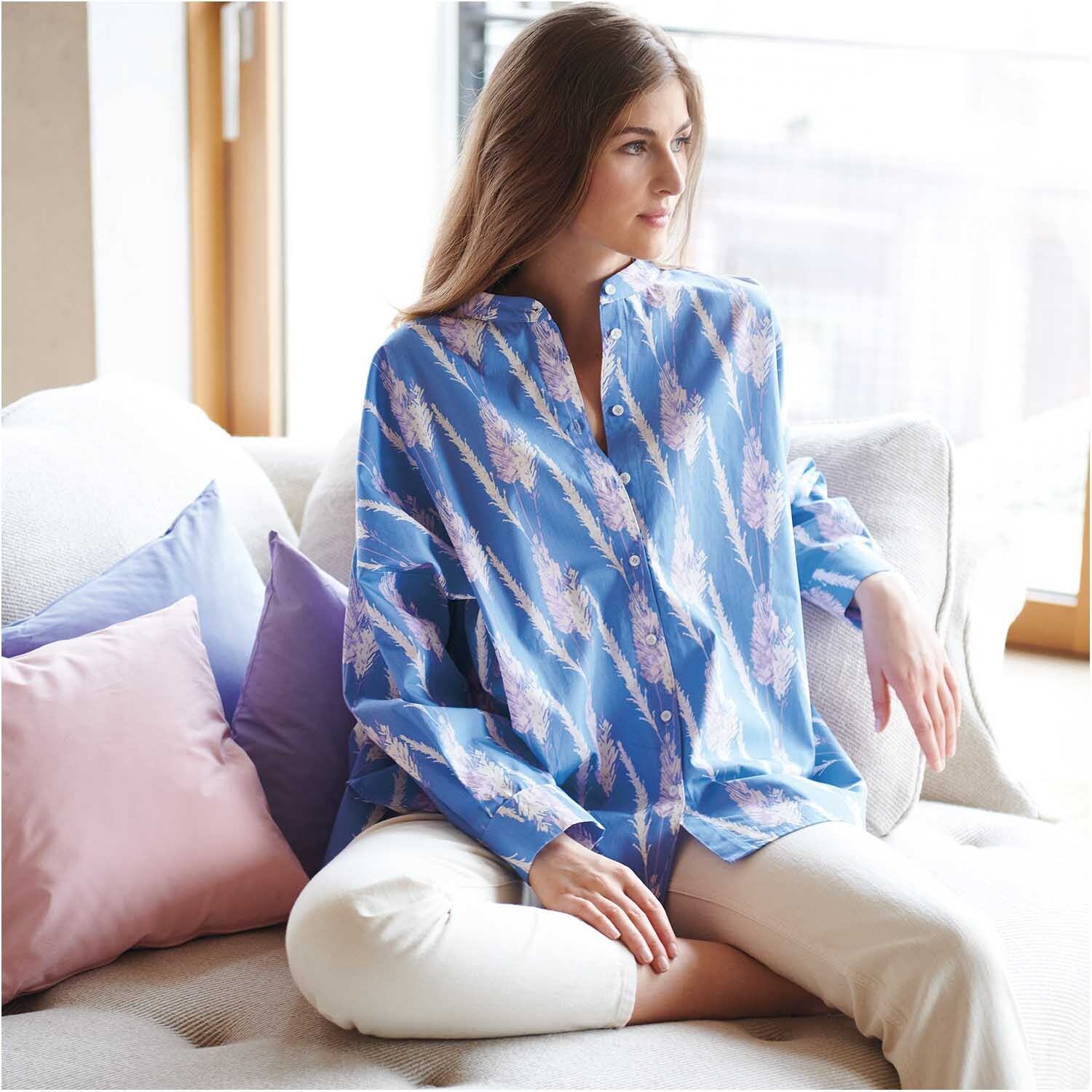 Meterware Druckstoff Pampasgras azur: Frau in azurblauer Bluse mit Pampasgras-Muster auf Sofa.